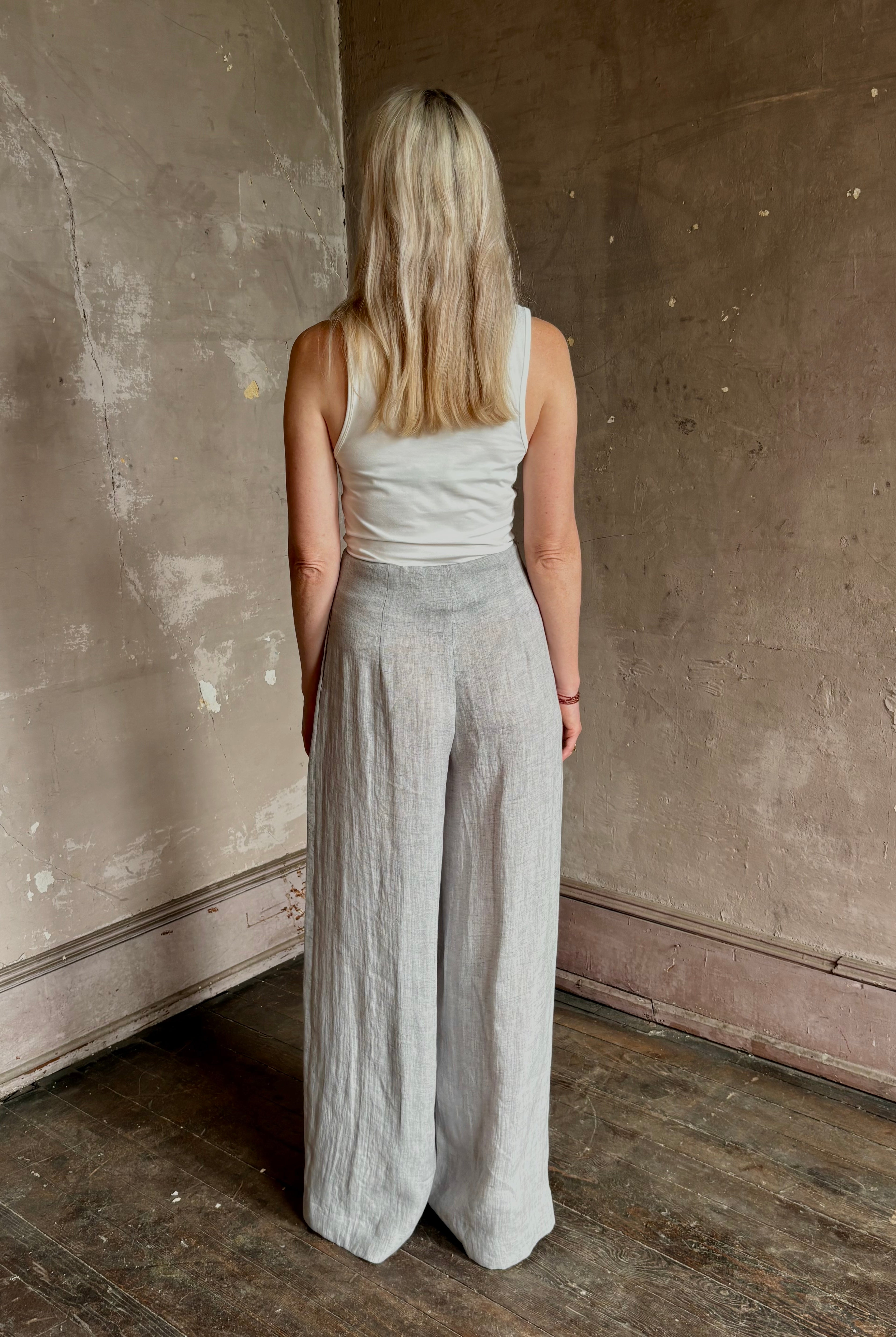 Mature woman wearing effortless women's designer Drew wide leg Trouser from TWP rendered in a versatile light heather grey and crafted from light weight hemp with high-rise, drop waist pleats, and side seam pockets, and made in the USA
