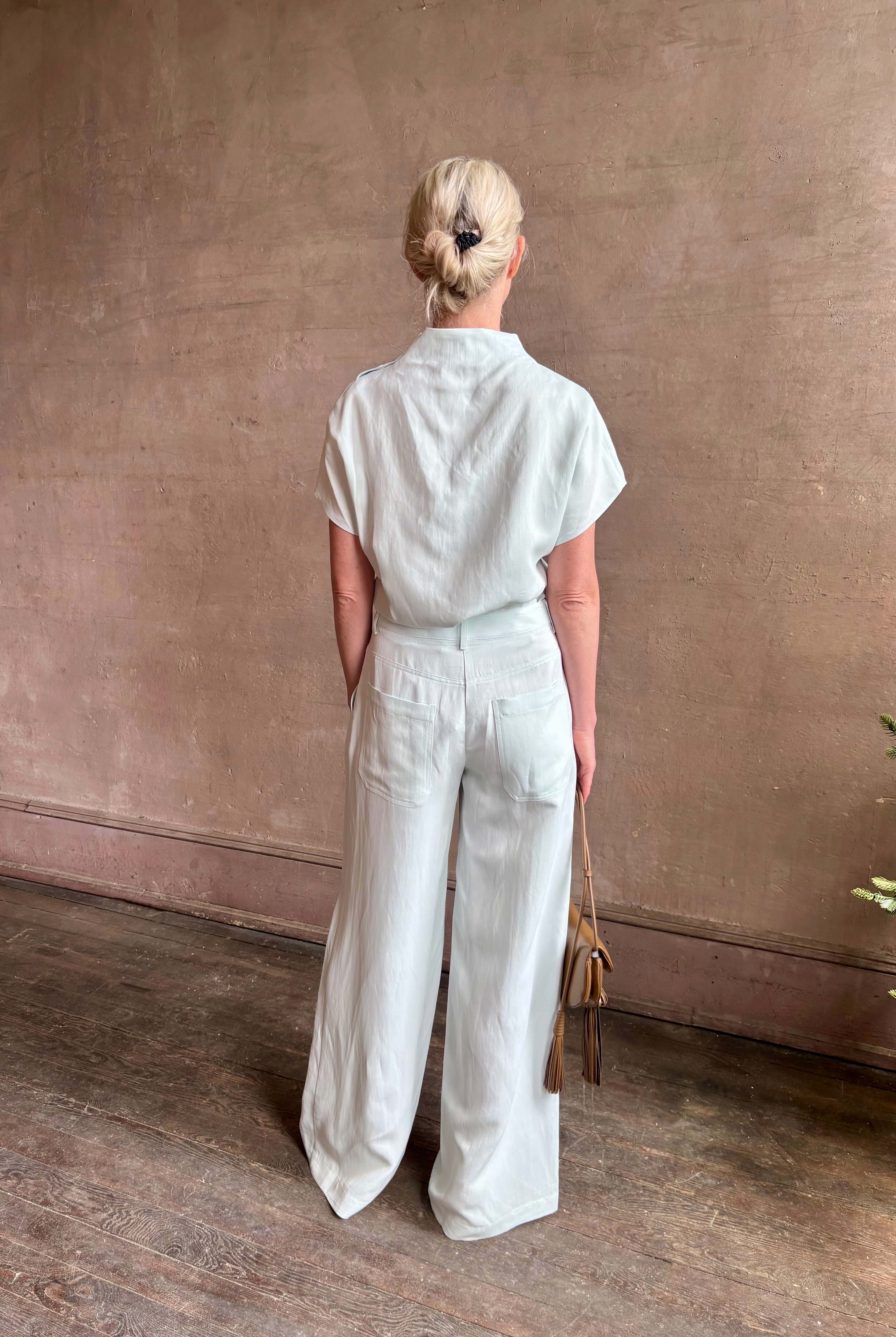Mature woman wearing the Dylan Pant from TWP rendered in a sea glass blue hue and crafted from a viscose and linen blend, made in the USA, this luxury mid-rise trouser offers a wide leg silhouette with hidden seam side and back pockets