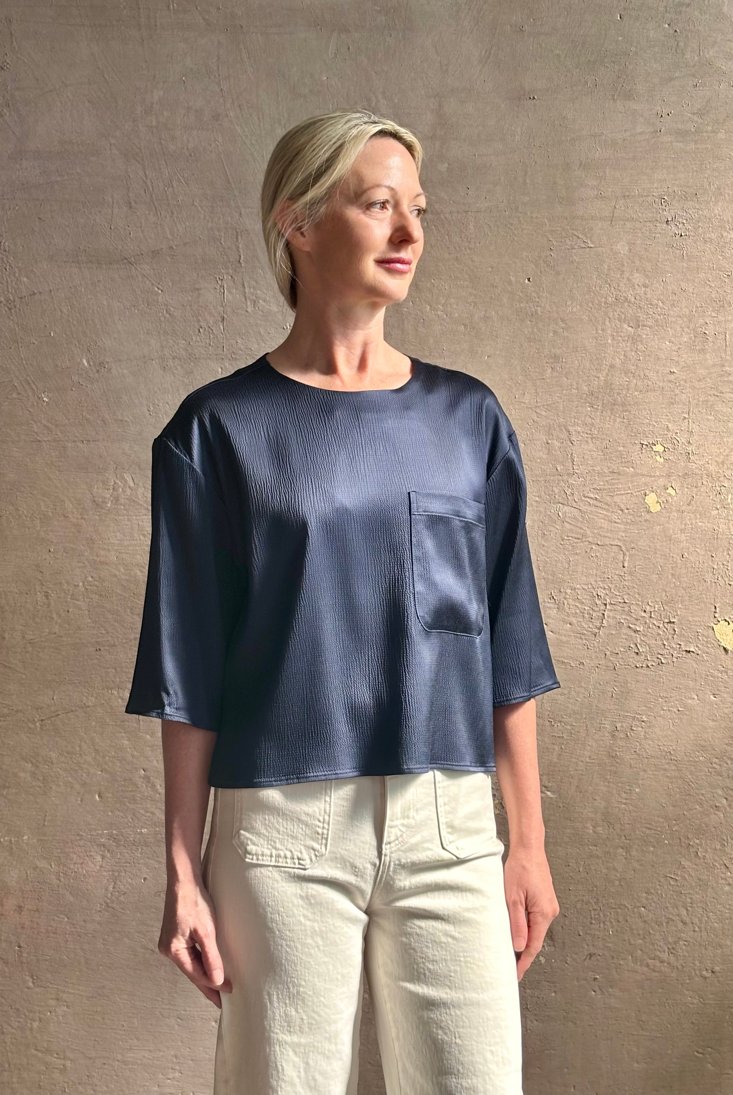 Mature woman wearing Women's luxury clothing brand TWP Ex T in premium hammered satin with short sleeves crew neck and a casual front pocket rendered in a beautiful navy blue hue