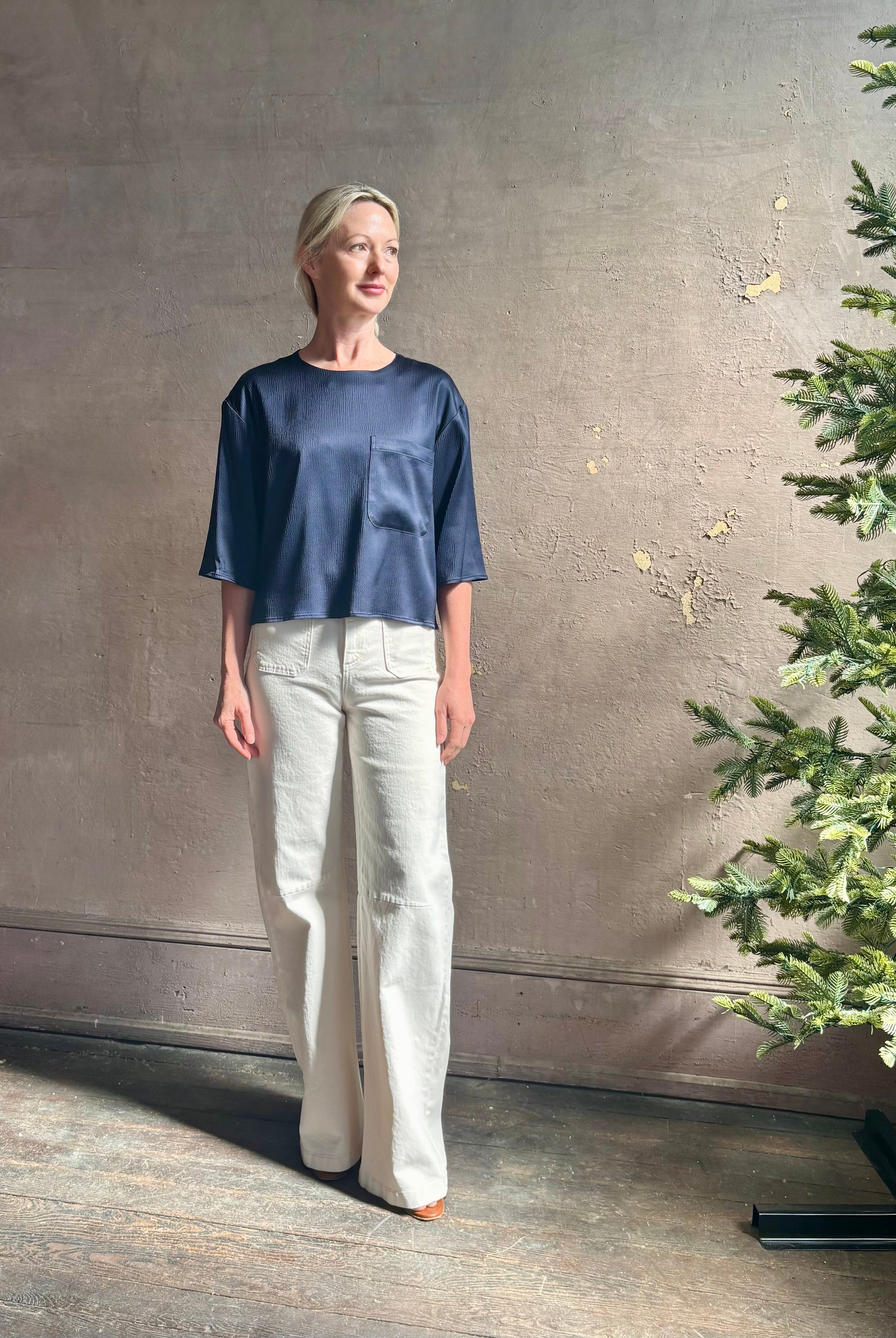 Mature woman wearing Women's luxury clothing brand TWP Ex T in premium hammered satin with short sleeves crew neck and a casual front pocket rendered in a beautiful navy blue hue