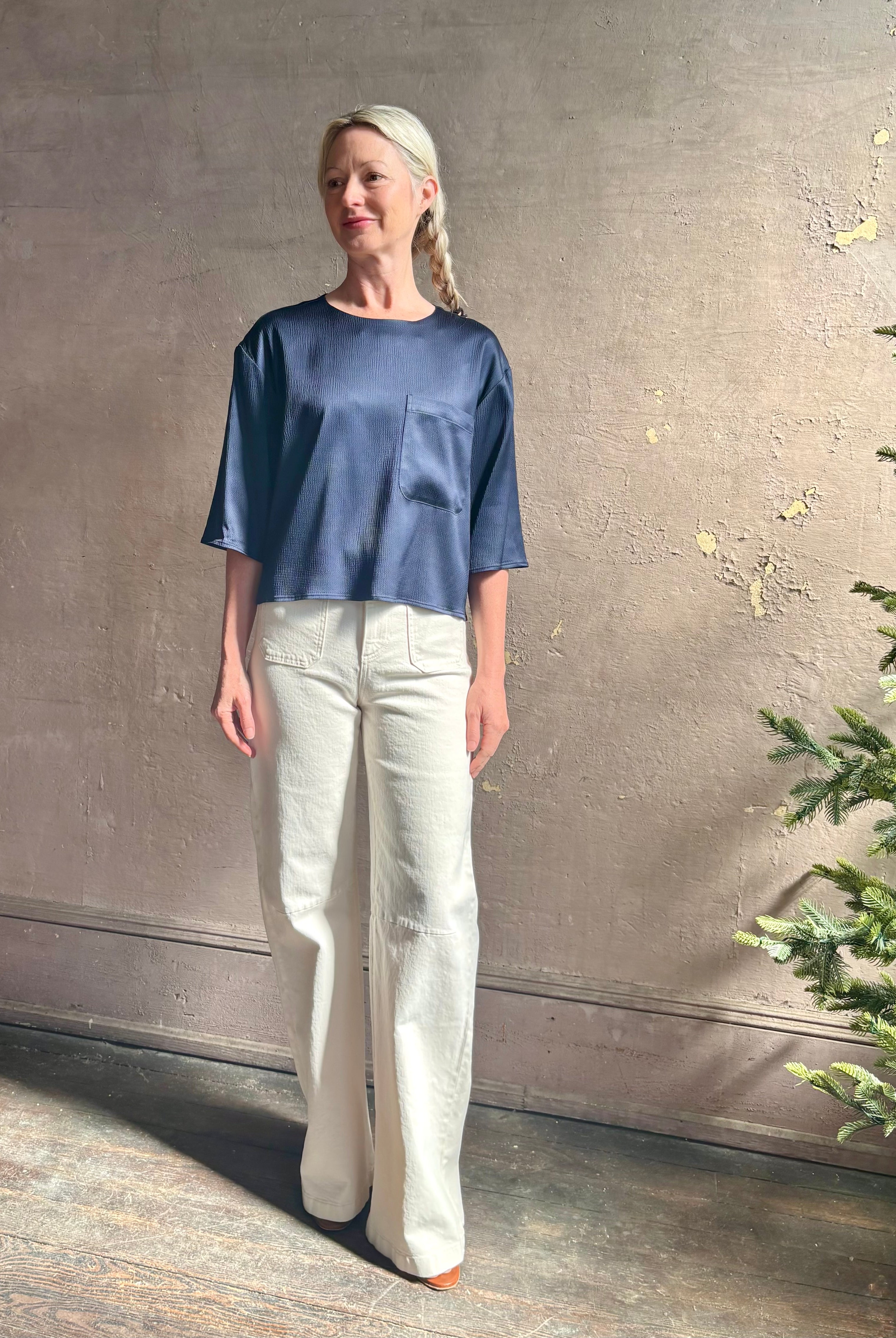 Mature woman wearing Women's luxury clothing brand TWP Ex T in premium hammered satin with short sleeves crew neck and a casual front pocket rendered in a beautiful navy blue hue
