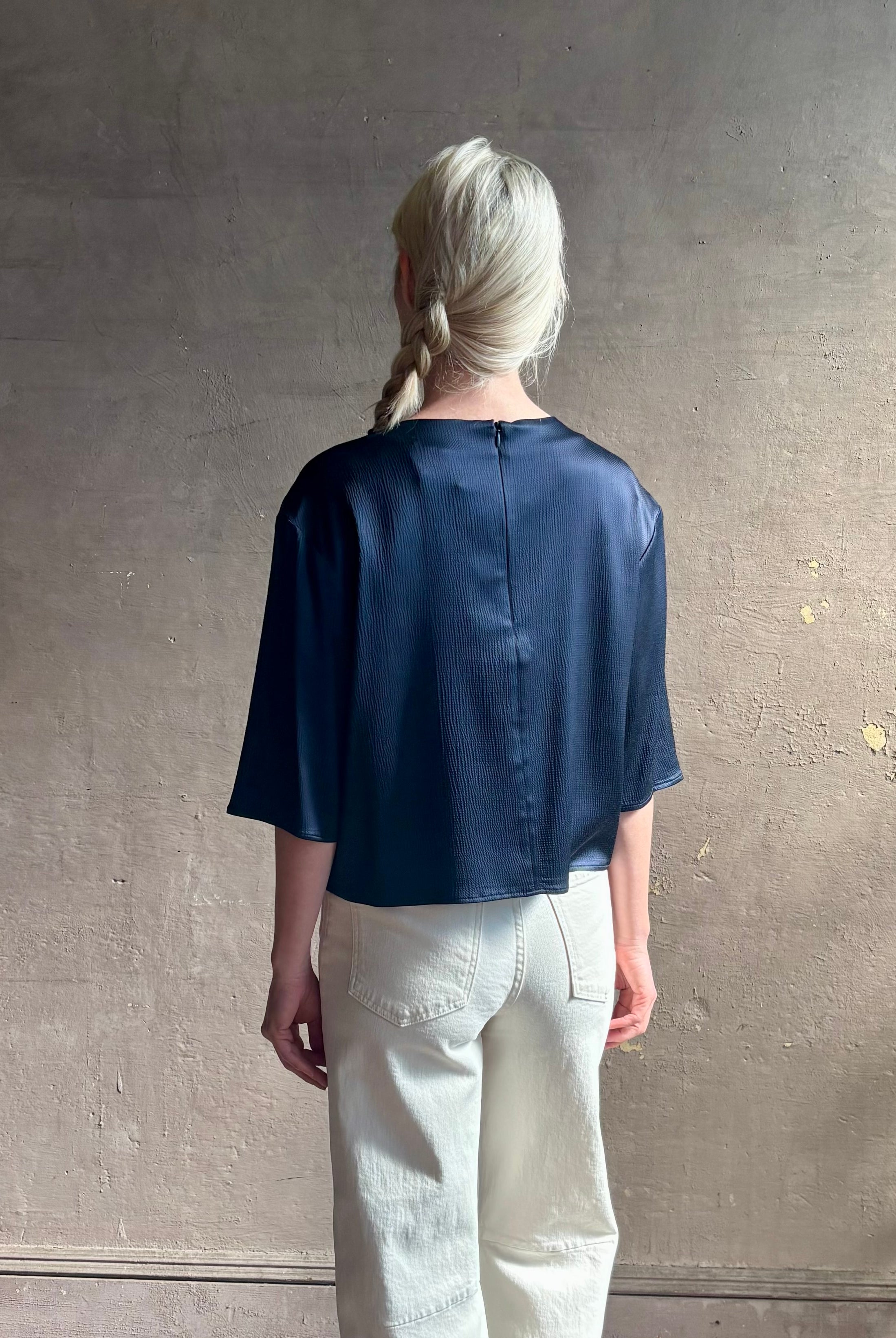 Mature woman wearing Women's luxury clothing brand TWP Ex T in premium hammered satin with short sleeves crew neck and a casual front pocket rendered in a beautiful navy blue hue