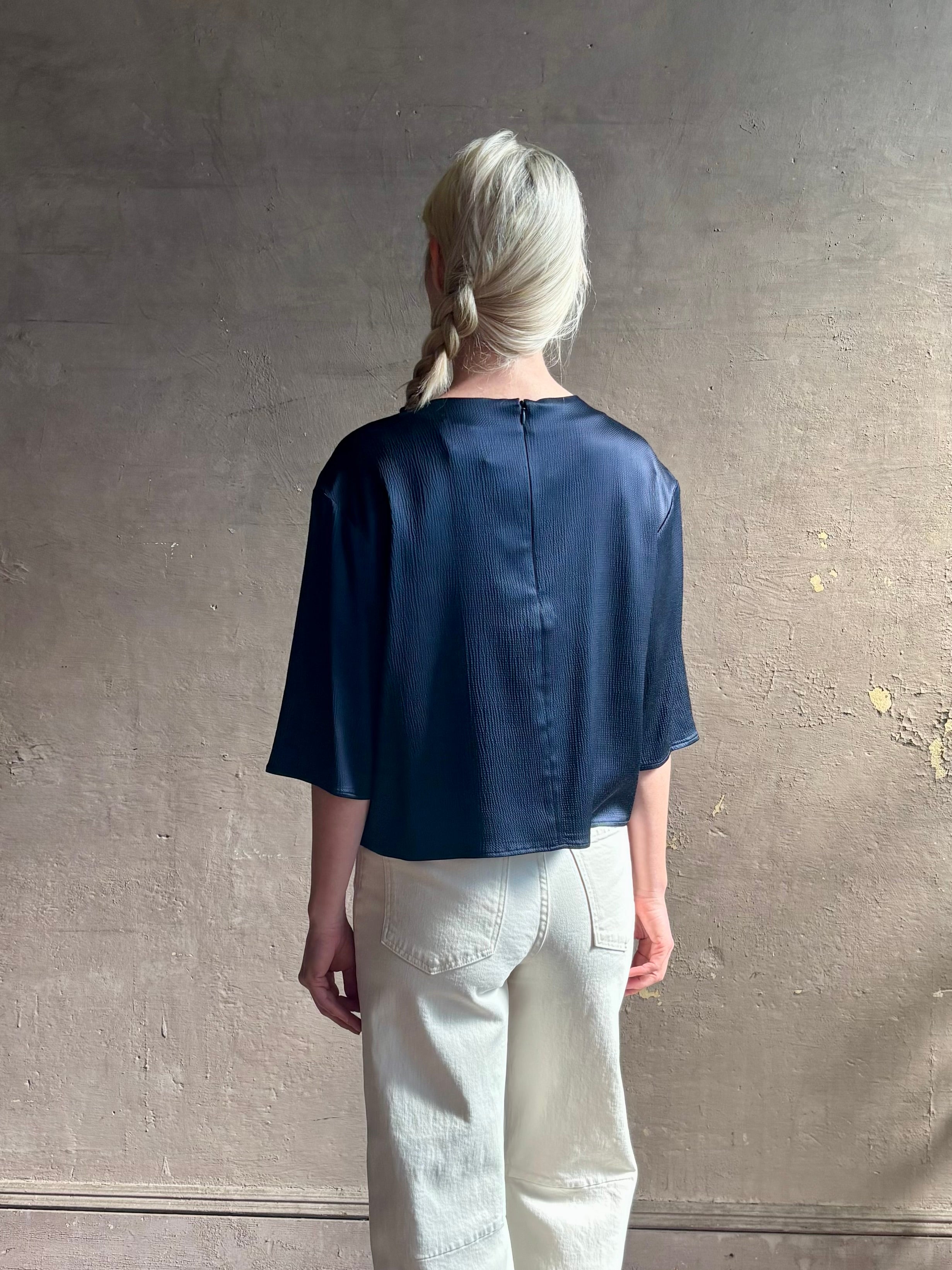 Mature woman wearing Women's luxury clothing brand TWP Ex T in premium hammered satin with short sleeves crew neck and a casual front pocket rendered in a beautiful navy blue hue