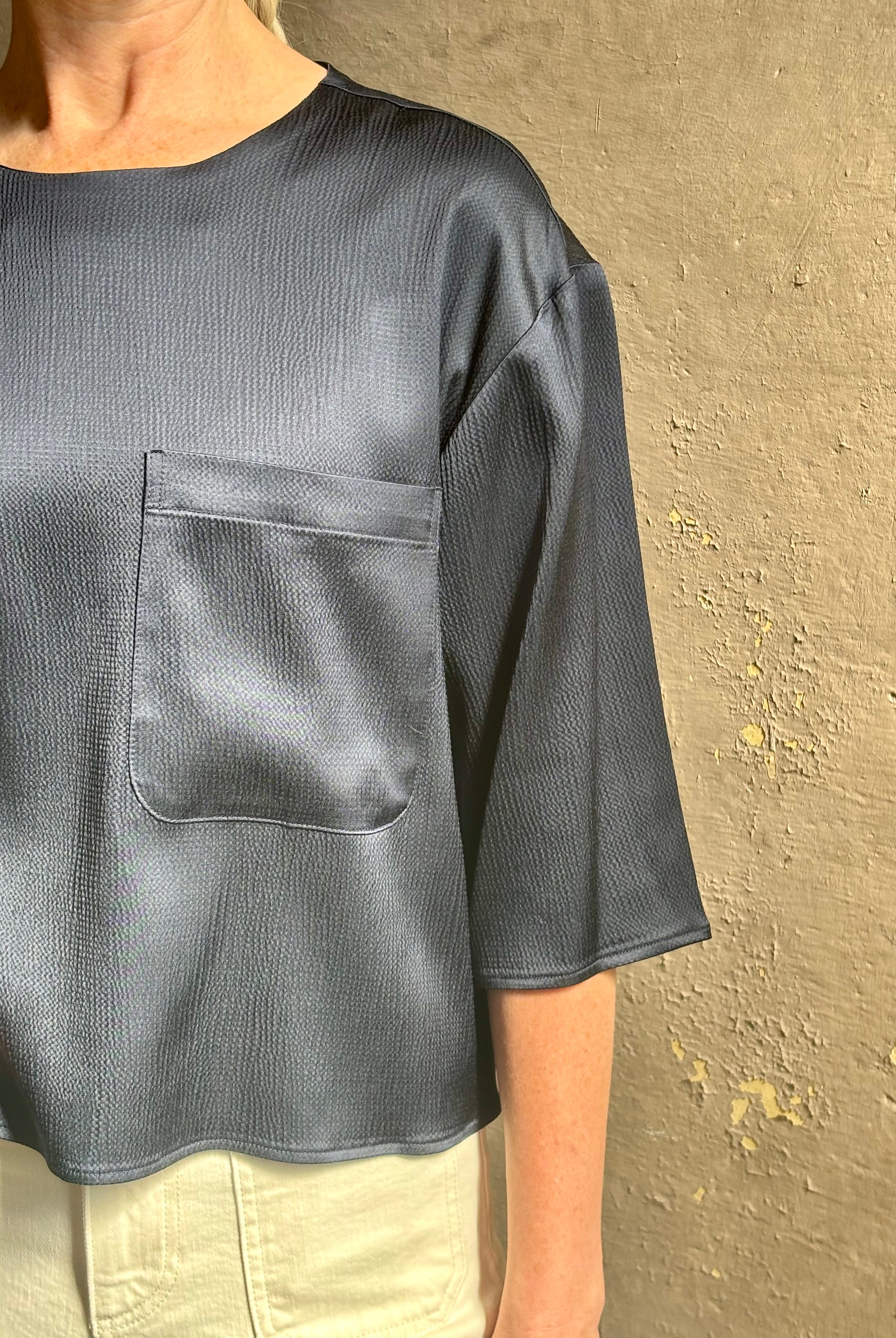 Mature woman wearing Women's luxury clothing brand TWP Ex T in premium hammered satin with short sleeves crew neck and a casual front pocket rendered in a beautiful navy blue hue