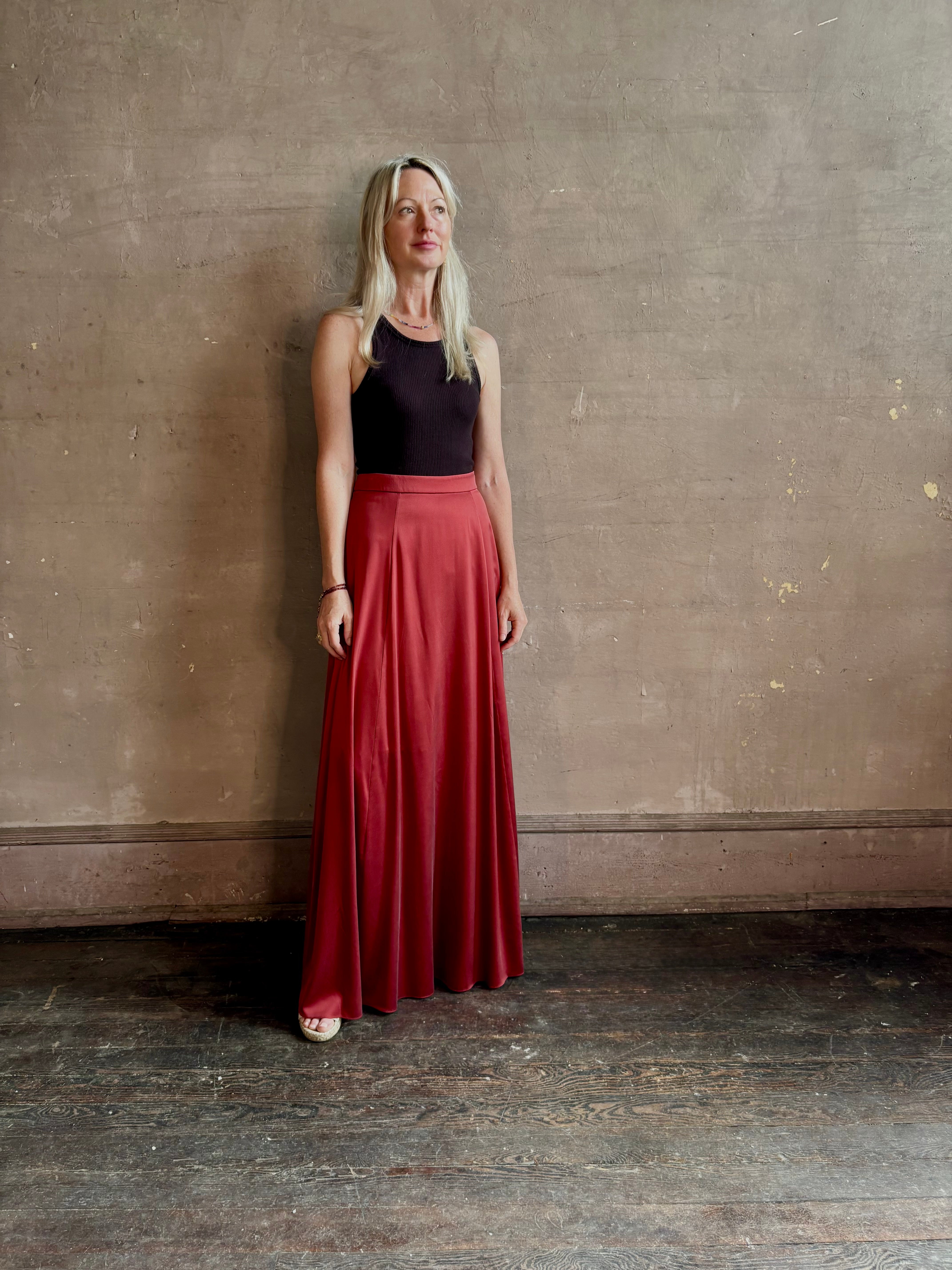 Mature woman wearing Flowy Maxi A-Line Skirt from TWP rendered in a rich red currant and crafted from a luxurious silk blend with hidden seam zip closure and tailored waistband