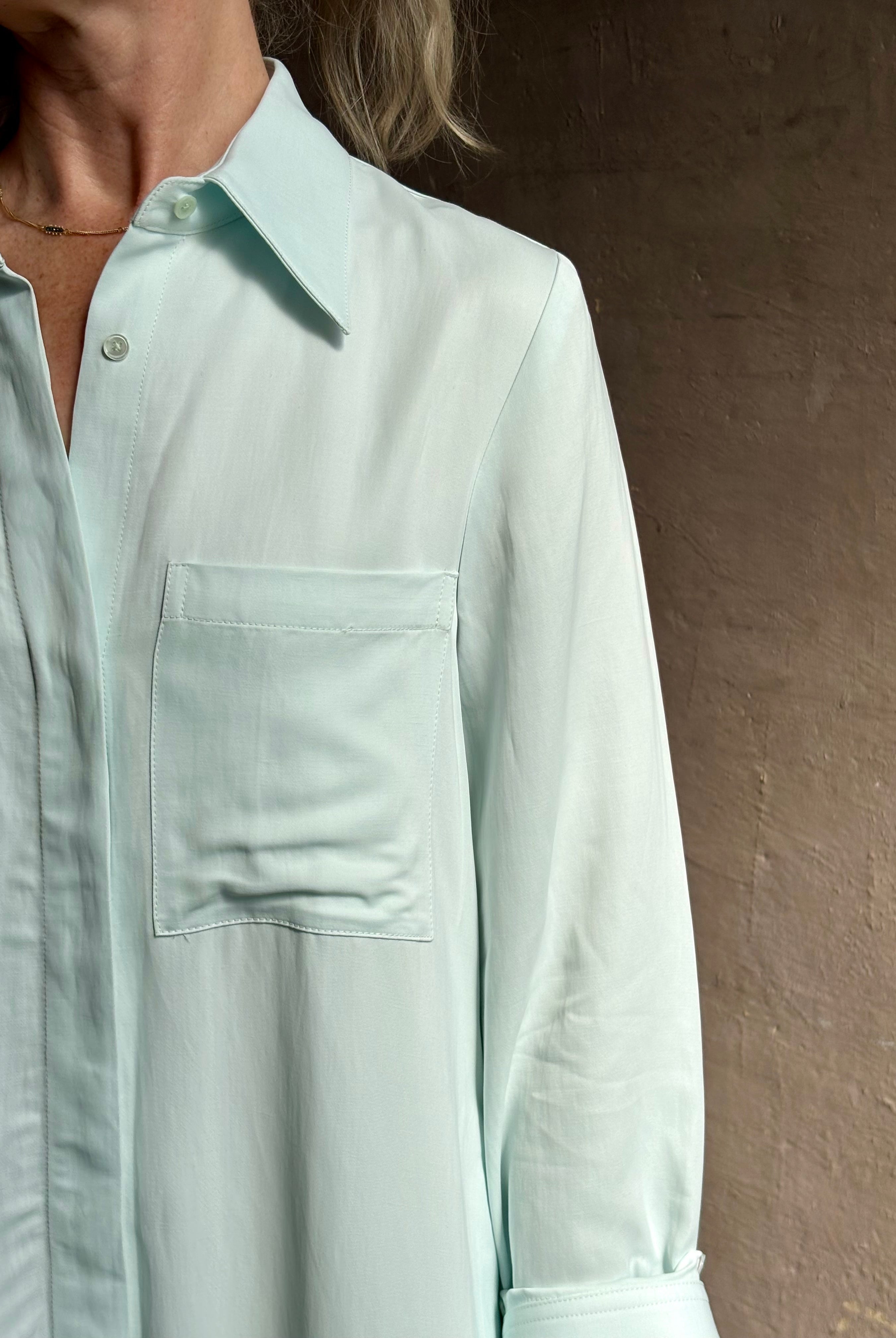 Mature woman wearing floor-length Jenny's Gown from TWP rendered in a sea glass hue and crafted from a viscose linen blend with beautiful draping, long sleeves, button front and cool girl loose fit