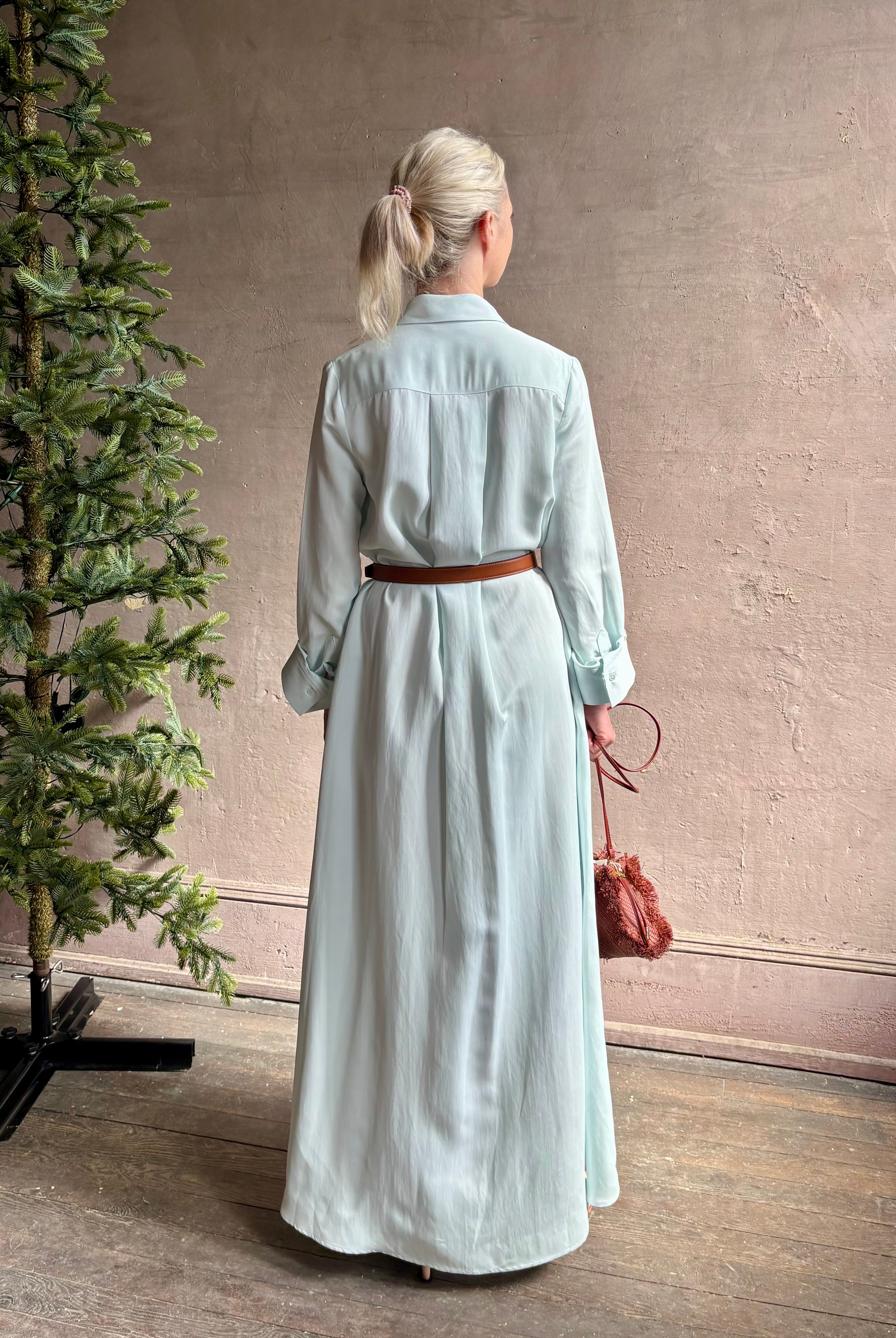 Mature woman wearing floor-length Jenny's Gown from TWP rendered in a sea glass hue and crafted from a viscose linen blend with beautiful draping, long sleeves, button front and cool girl loose fit