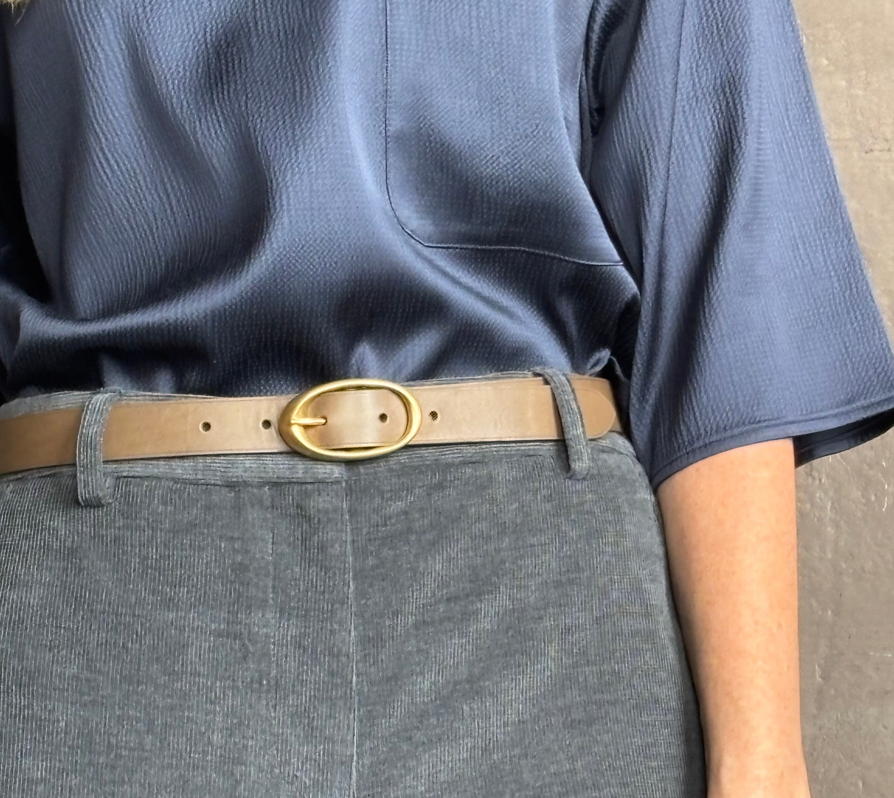 Close up image of woman wearing TWP narrow belt in mink light brown colorway and fabricated with premium leather and brass oval buckle