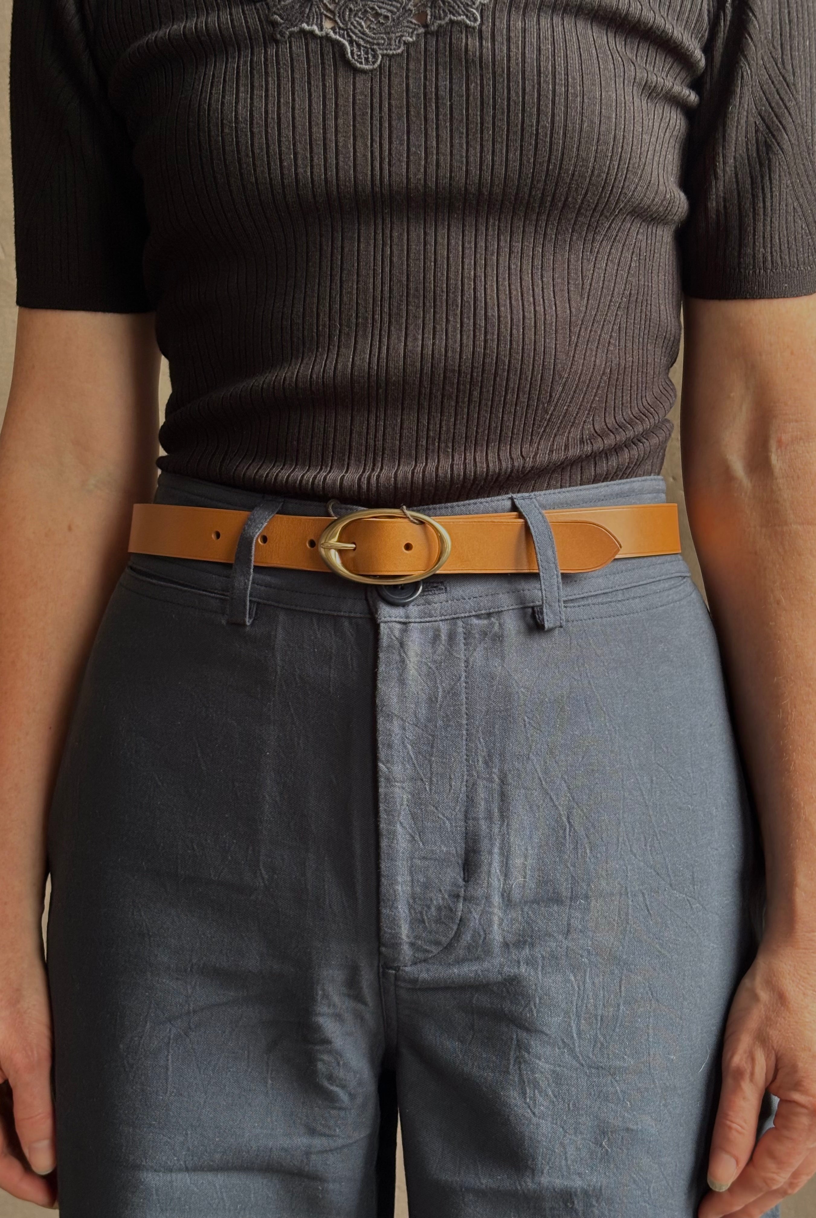 Mature woman wearing a TWP vintage camel brown narrow leather belt with warm gold tone oval buckle