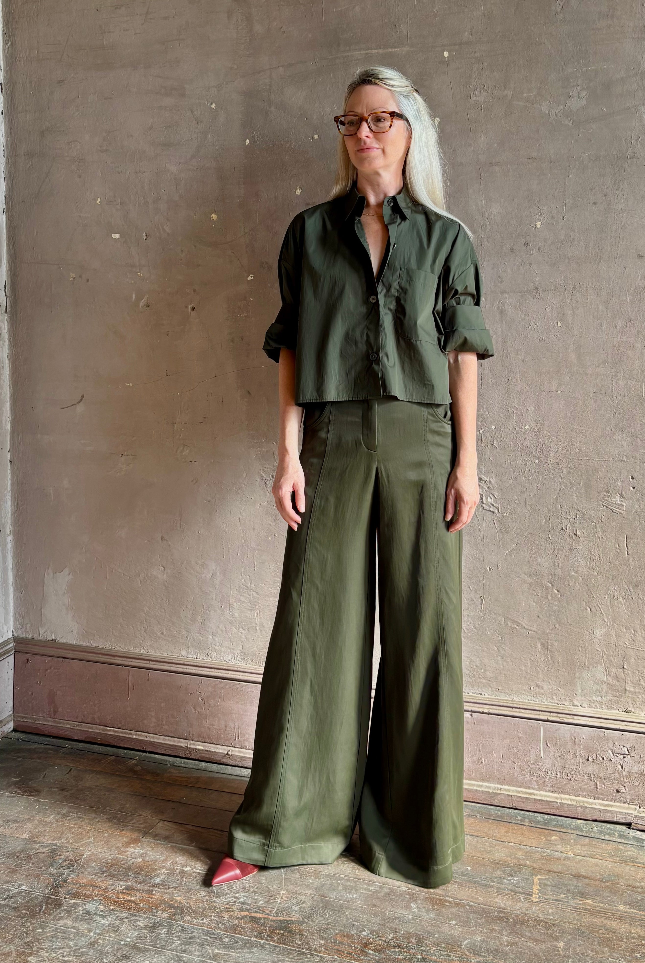 Mature woman wearing TWP next ex cotton poplin dark green rosin button-up shirt with rolled sleeves and collar