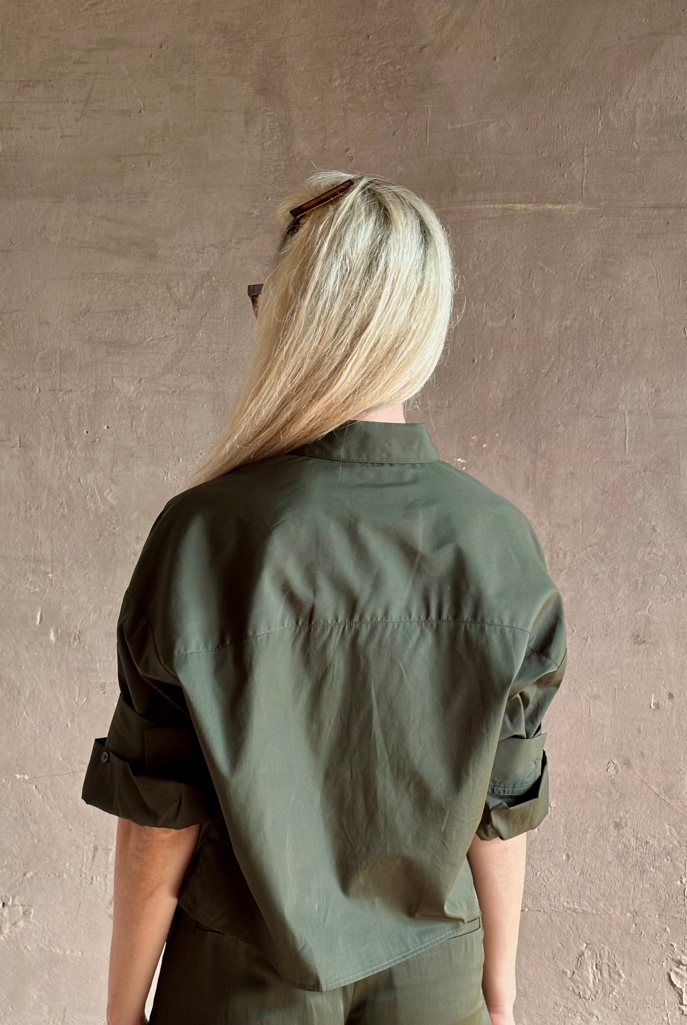 Mature woman wearing TWP next ex cotton poplin dark green rosin button-up shirt with rolled sleeves and collar