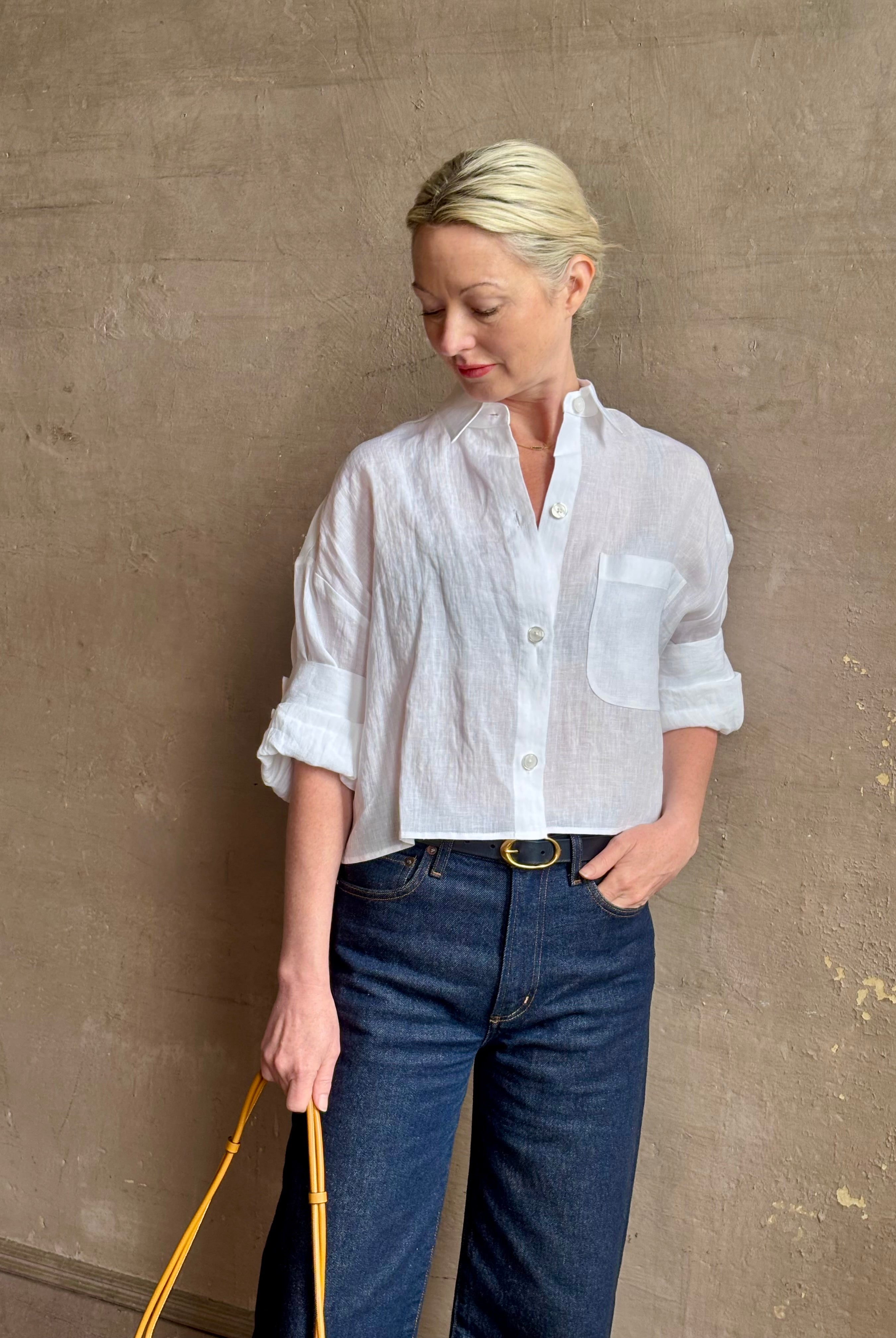 Mature woman wearing the Next Ex Top from TWP rendered in a crisp white and crafted from premium linen in New York City, this luxury linen top offers effortless cool girl with an intentionally oversized boxy silhouette with tailored half sleeve cuffs, collared button - down menswear inspired with a single front pocket