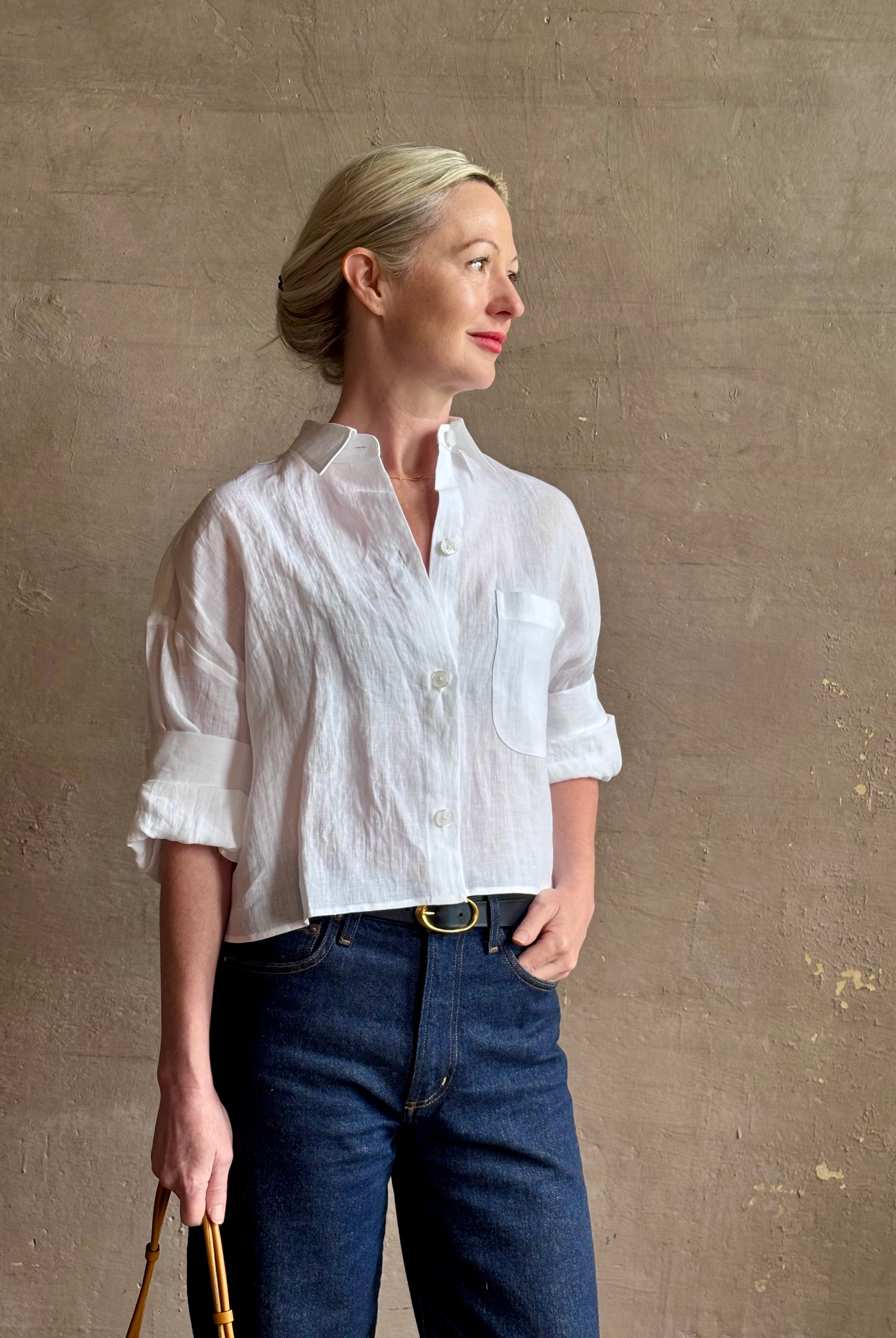 Mature woman wearing the Next Ex Top from TWP rendered in a crisp white and crafted from premium linen in New York City, this luxury linen top offers effortless cool girl with an intentionally oversized boxy silhouette with tailored half sleeve cuffs, collared button - down menswear inspired with a single front pocket