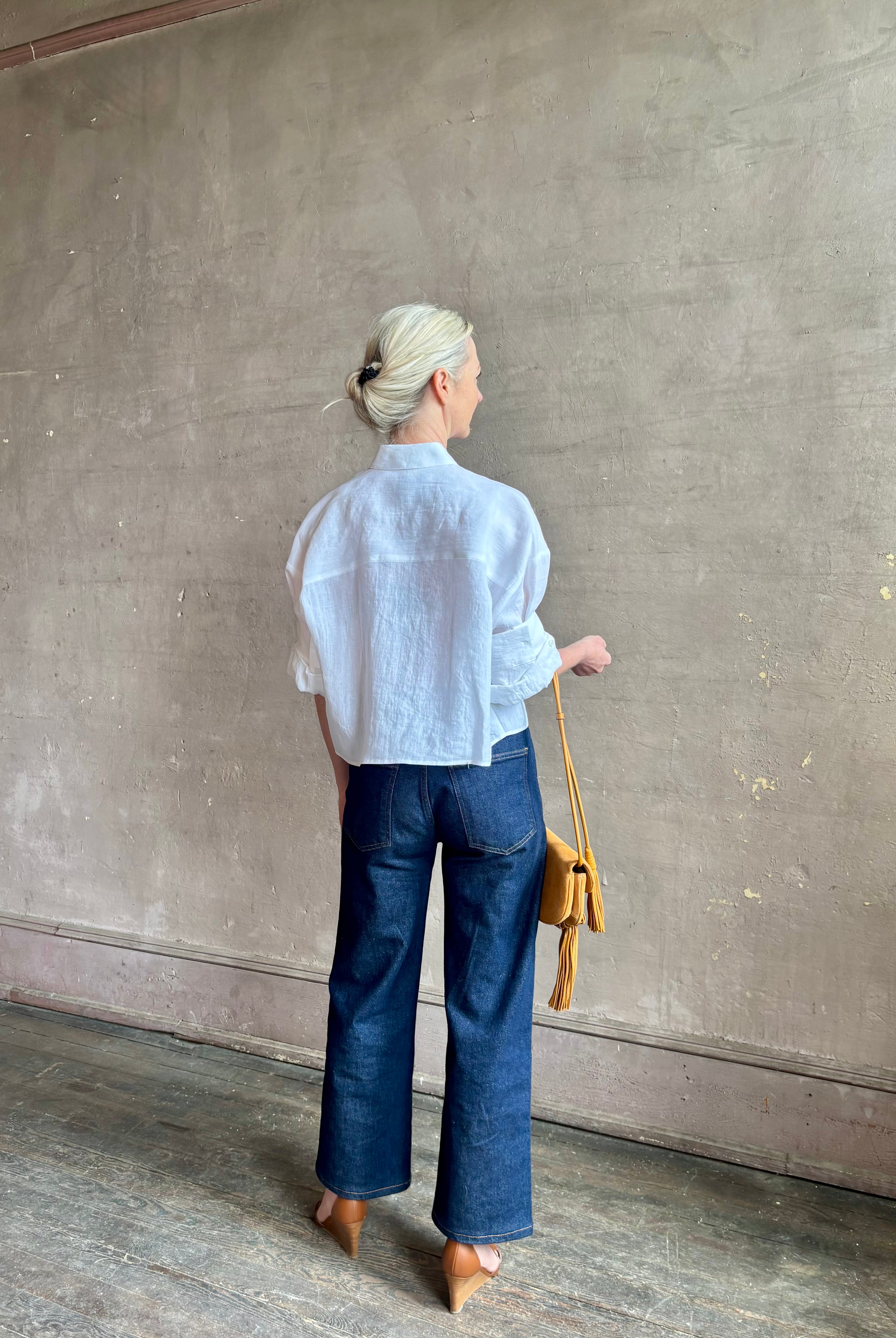 Mature woman wearing the Next Ex Top from TWP rendered in a crisp white and crafted from premium linen in New York City, this luxury linen top offers effortless cool girl with an intentionally oversized boxy silhouette with tailored half sleeve cuffs, collared button - down menswear inspired with a single front pocket