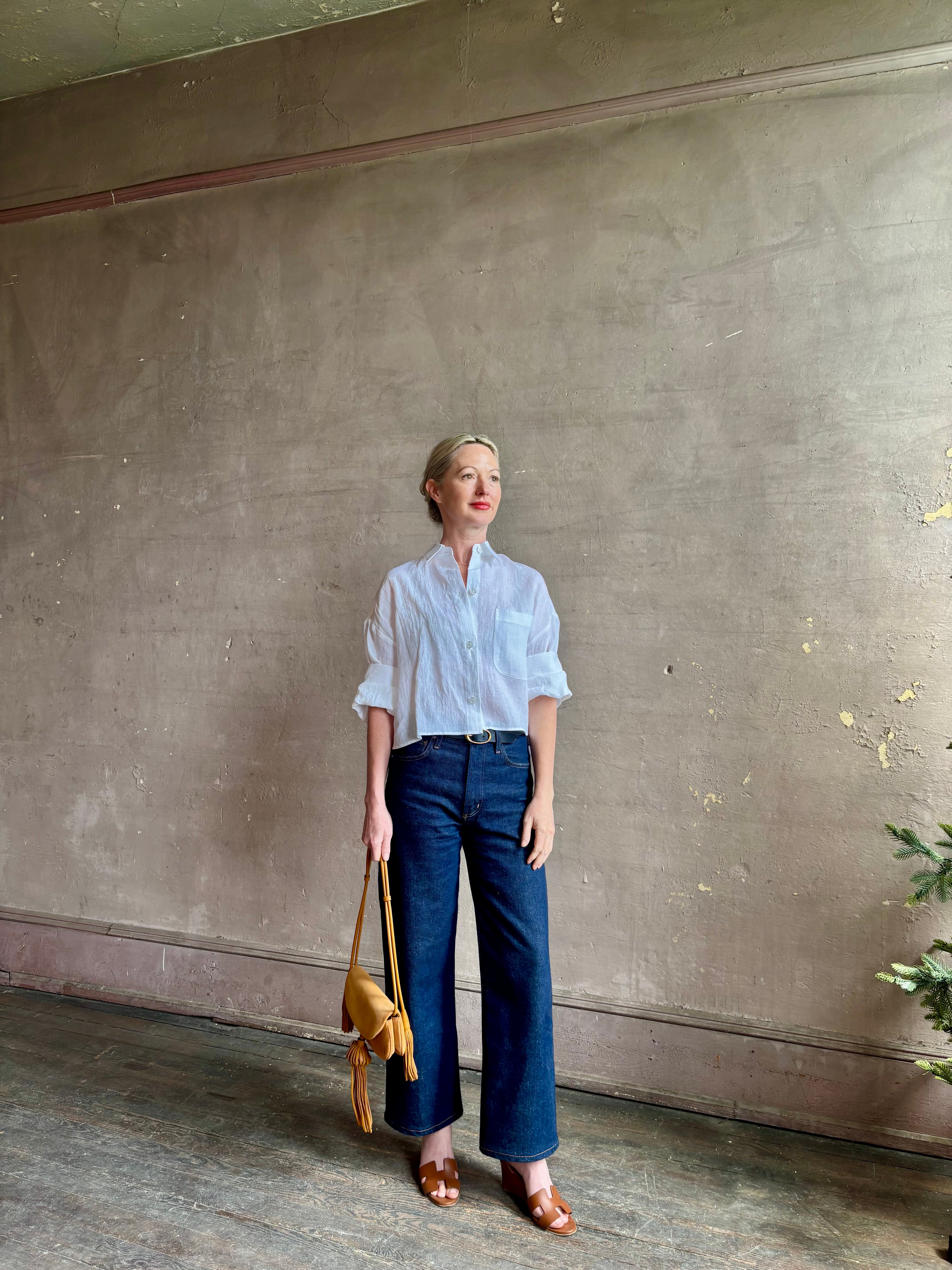 Mature woman wearing the Next Ex Top from TWP rendered in a crisp white and crafted from premium linen in New York City, this luxury linen top offers effortless cool girl with an intentionally oversized boxy silhouette with tailored half sleeve cuffs, collared button - down menswear inspired with a single front pocket