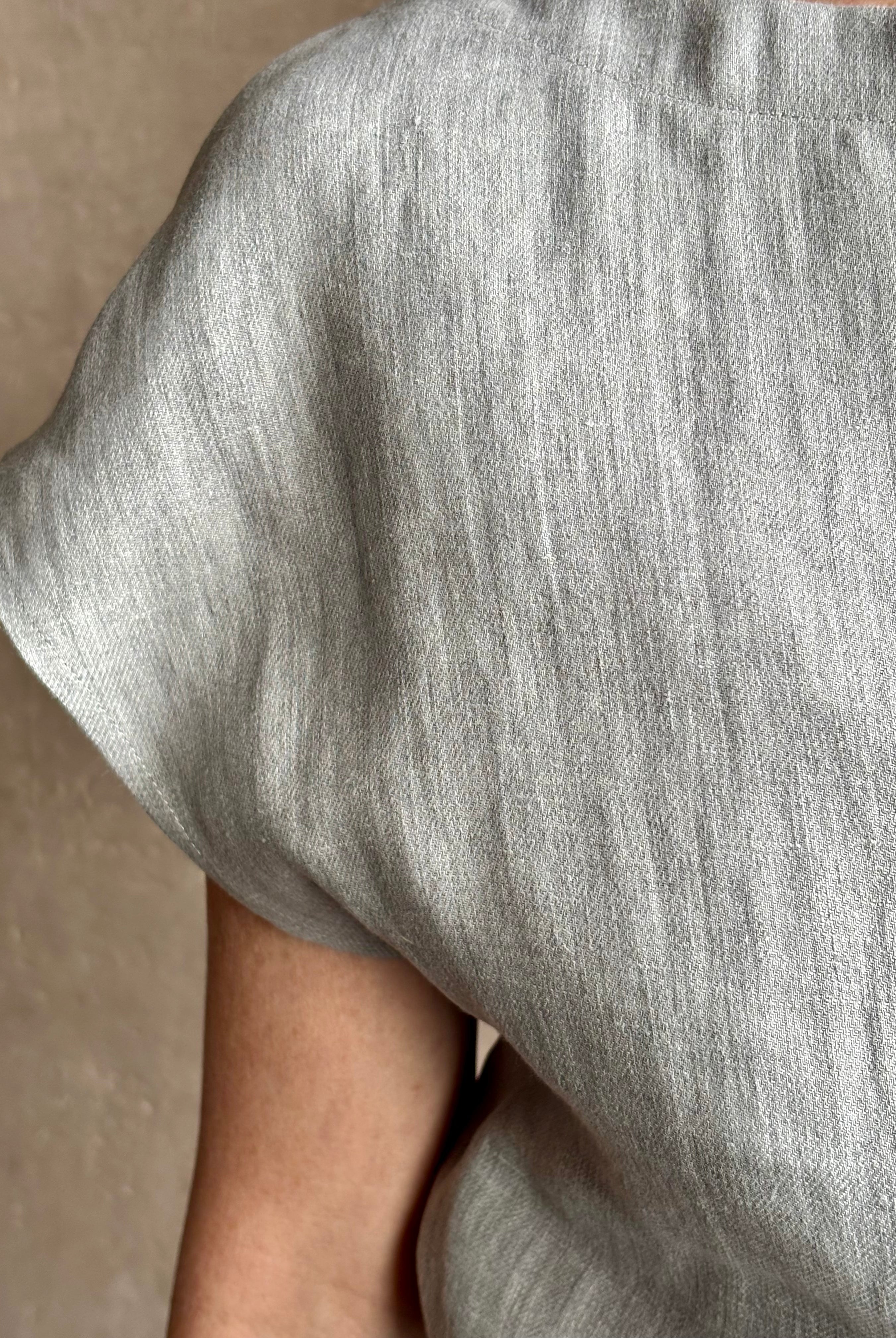 Mature woman wearing the Simple T Top from TWP that is rendered in a light heather grey hemp with short sleeves and boat neckline
