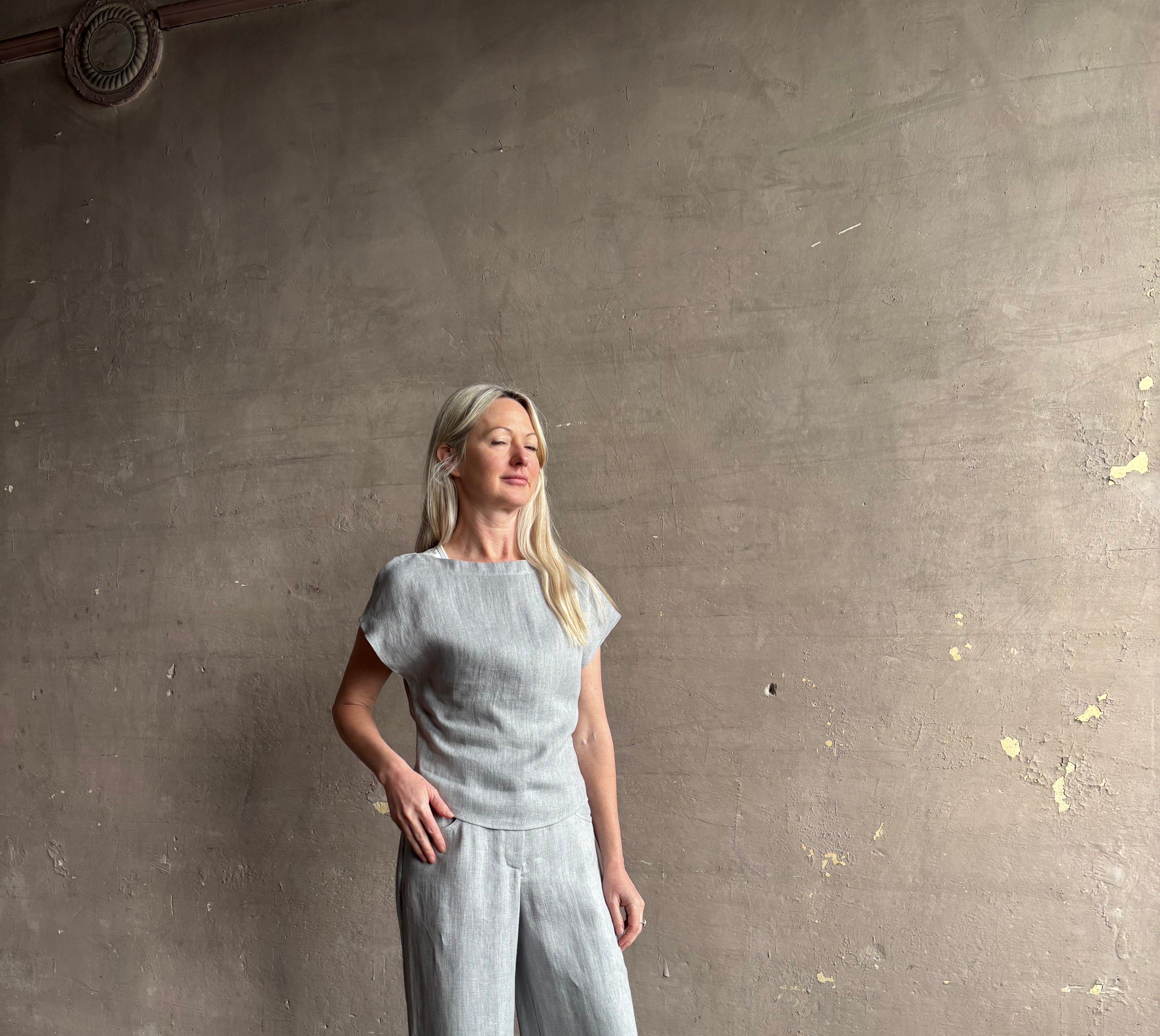 Mature woman wearing the Simple T Top from TWP that is rendered in a light heather grey hemp with short sleeves and boat neckline