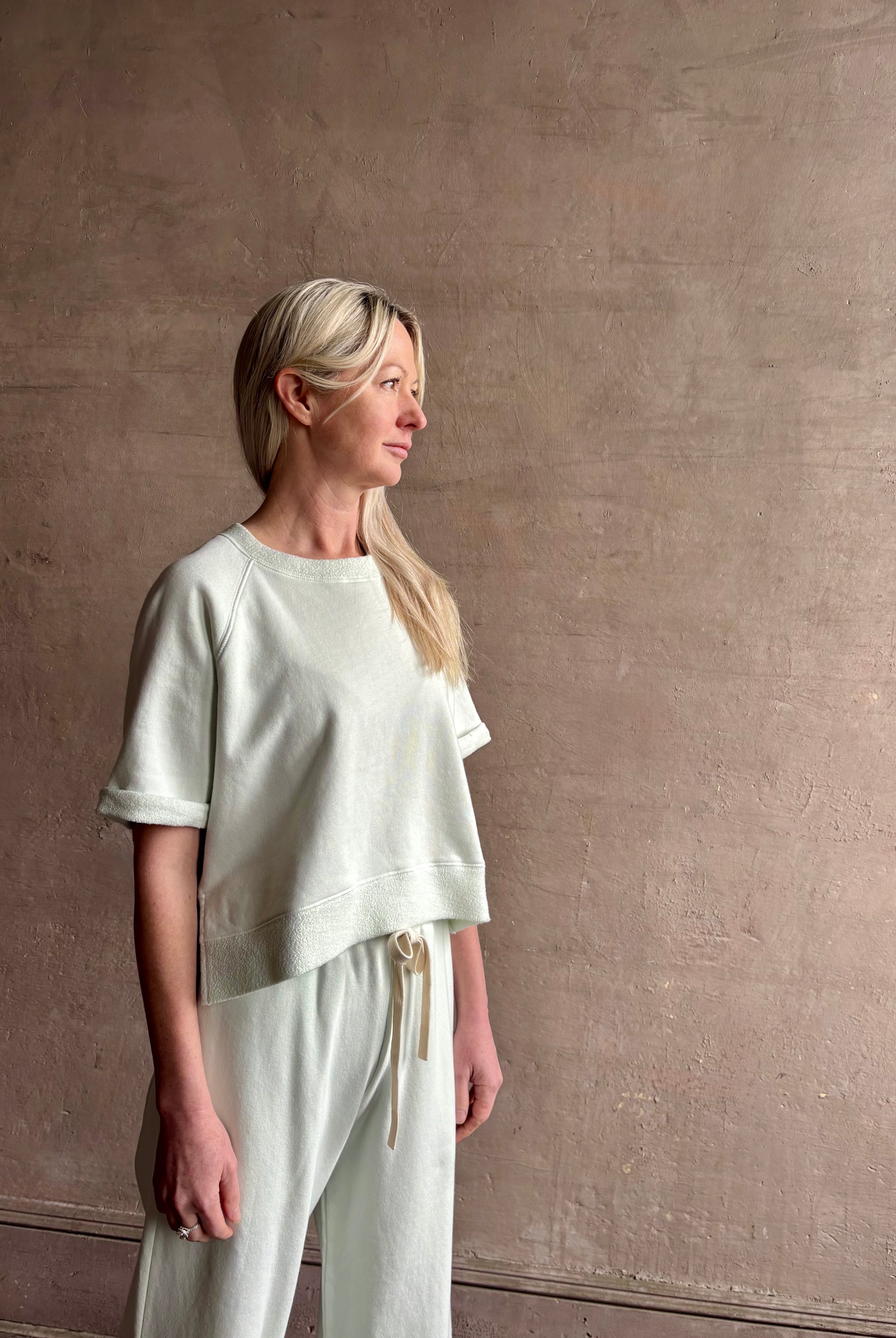 Mature woman wearing Slouchy Rolled Tee Top from TWP rendered in a sea glass hue and crafted from cotton with raglan short sleeves, crew neck and relaxed silhouette