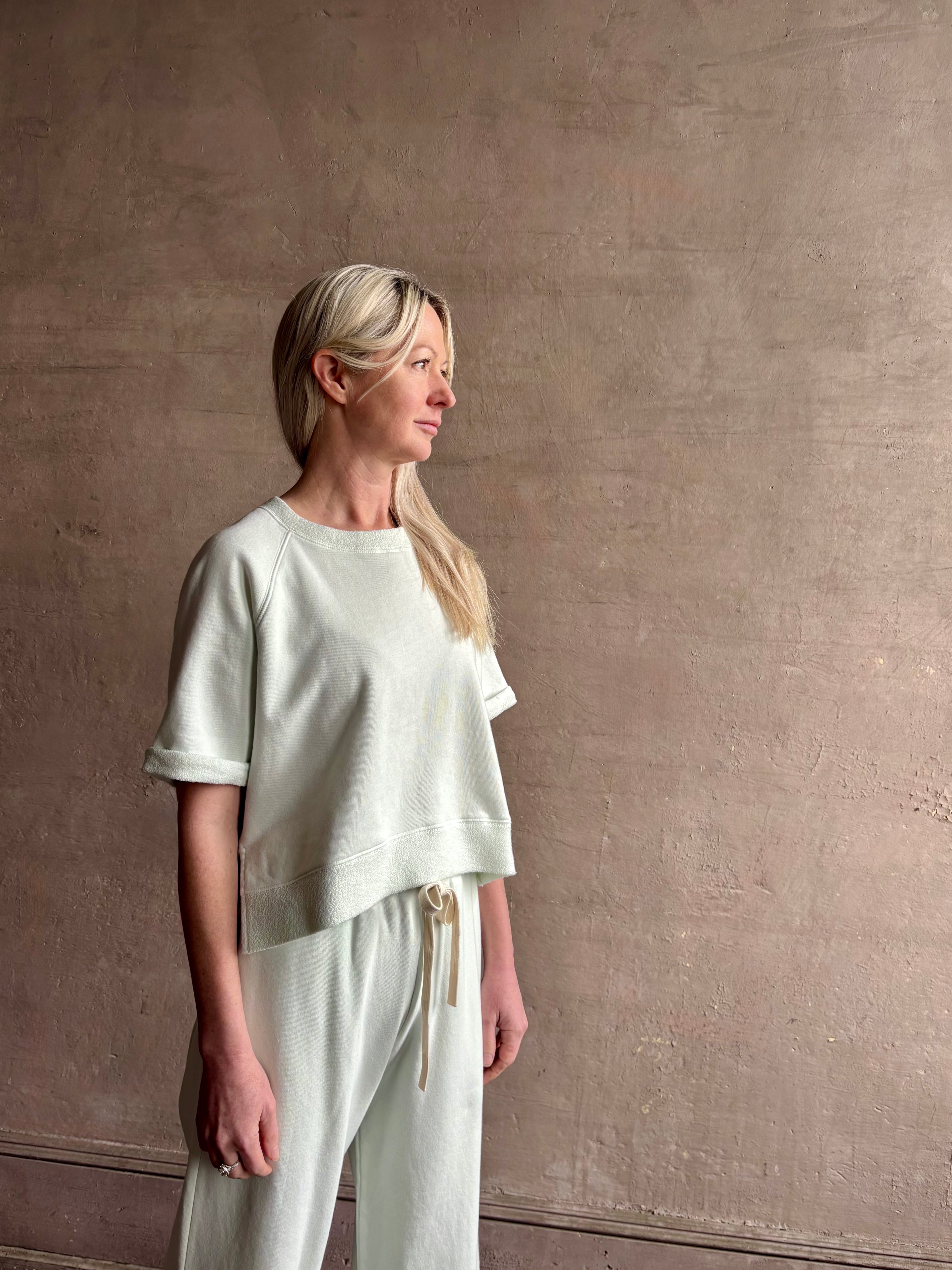 Mature woman wearing Slouchy Rolled Tee Top from TWP rendered in a sea glass hue and crafted from cotton with raglan short sleeves, crew neck and relaxed silhouette