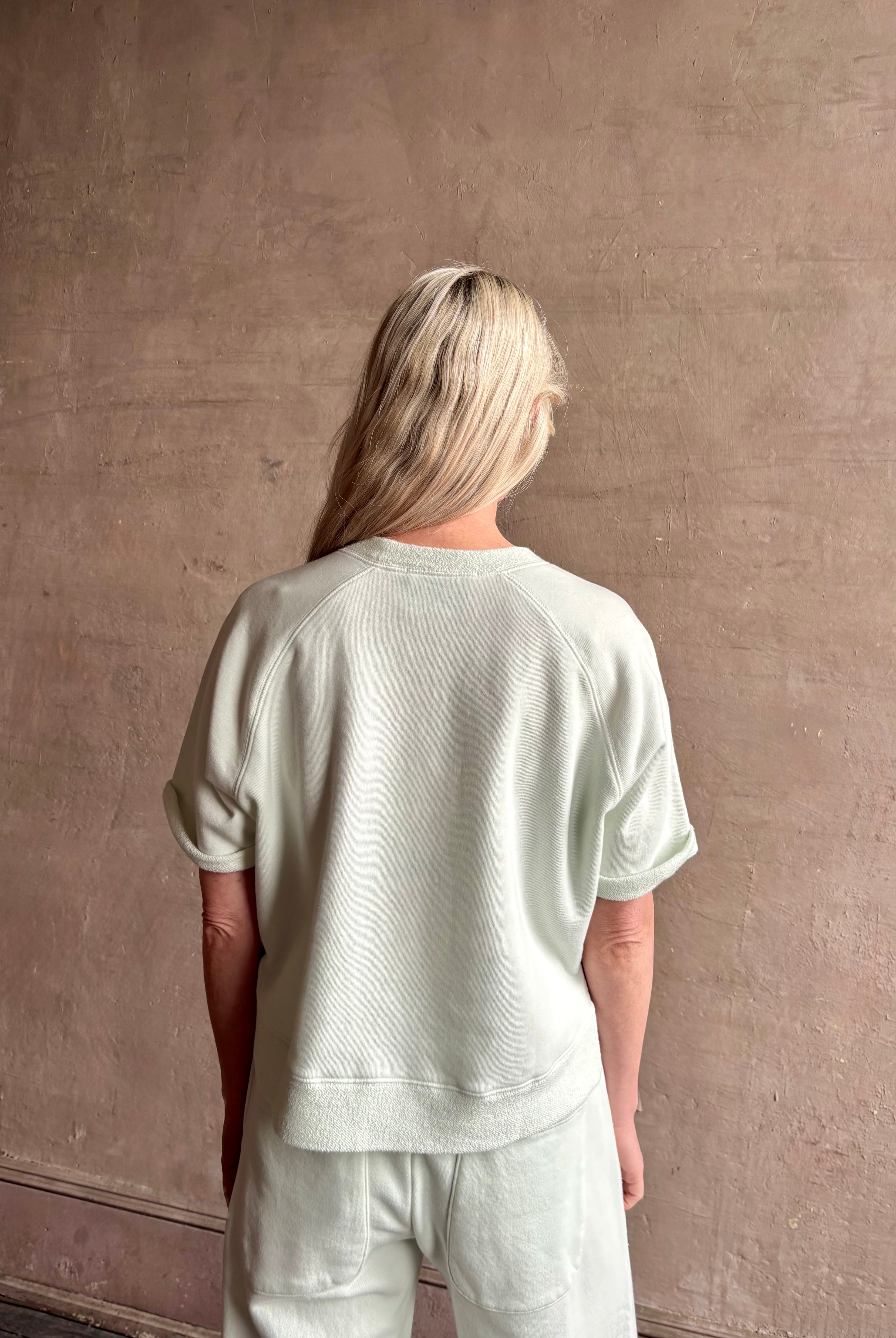 Mature woman wearing Slouchy Rolled Tee Top from TWP rendered in a sea glass hue and crafted from cotton with raglan short sleeves, crew neck and relaxed silhouette