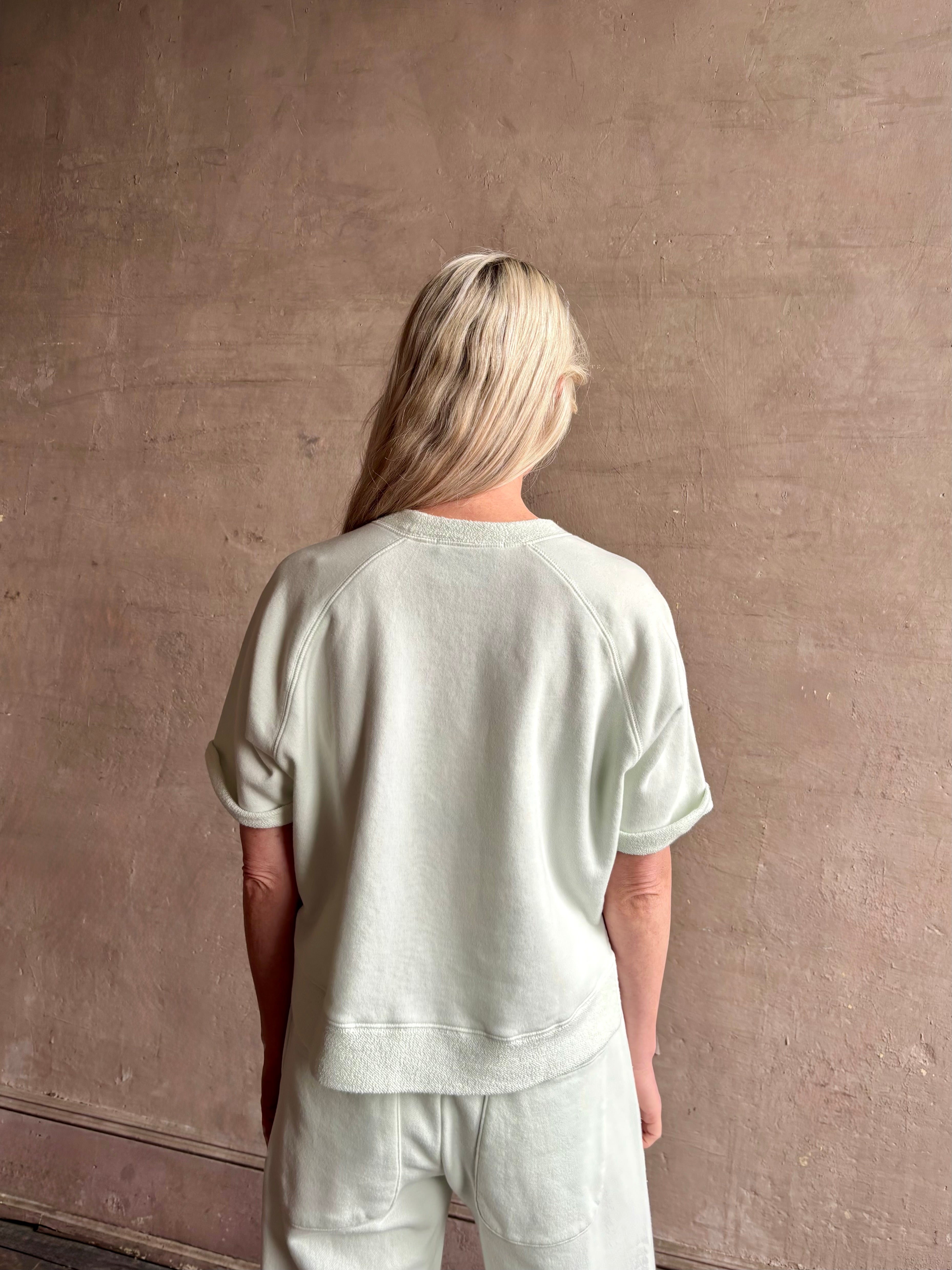 Mature woman wearing Slouchy Rolled Tee Top from TWP rendered in a sea glass hue and crafted from cotton with raglan short sleeves, crew neck and relaxed silhouette