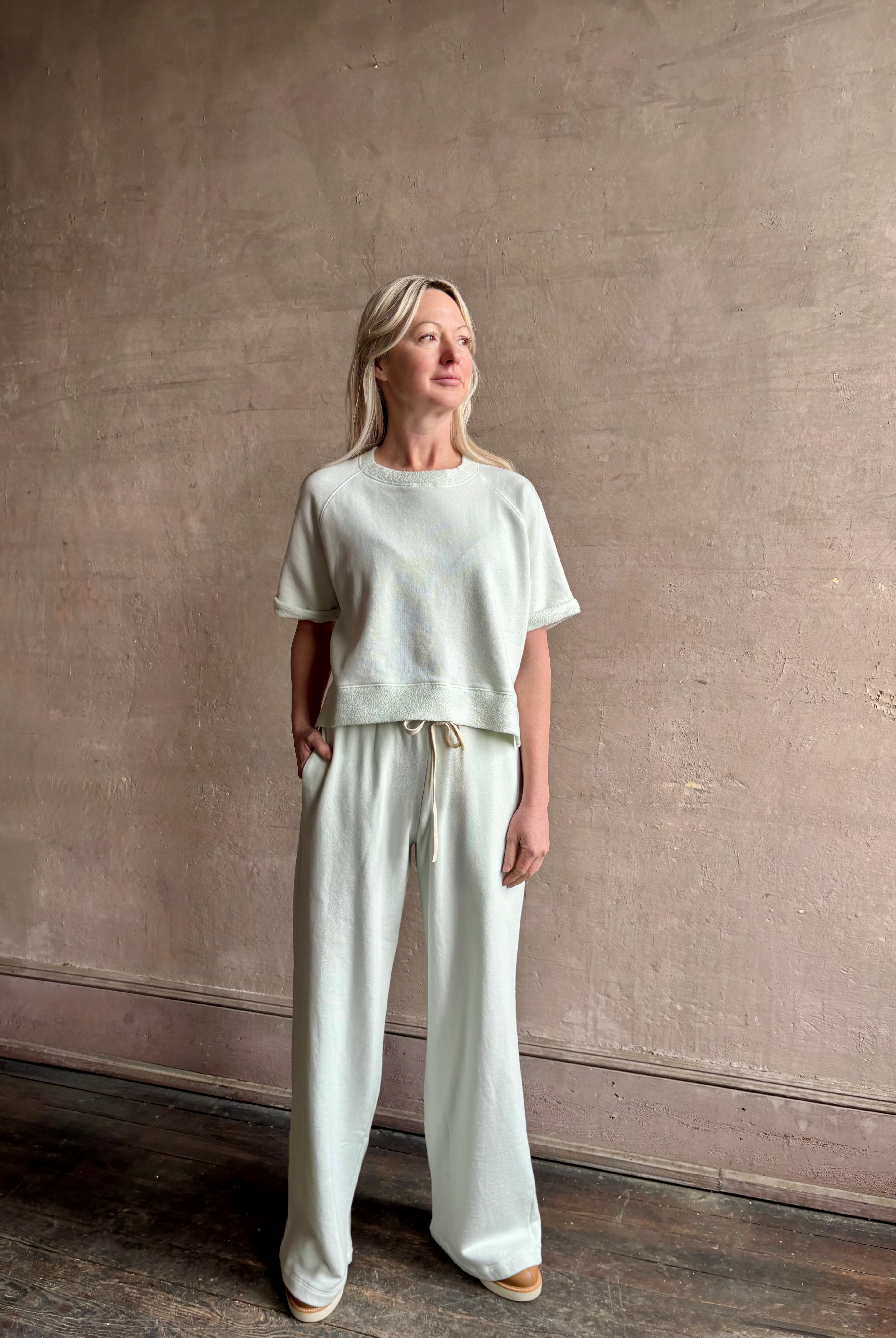 Mature woman wearing Slouchy Rolled Tee Top from TWP rendered in a sea glass hue and crafted from cotton with raglan short sleeves, crew neck and relaxed silhouette