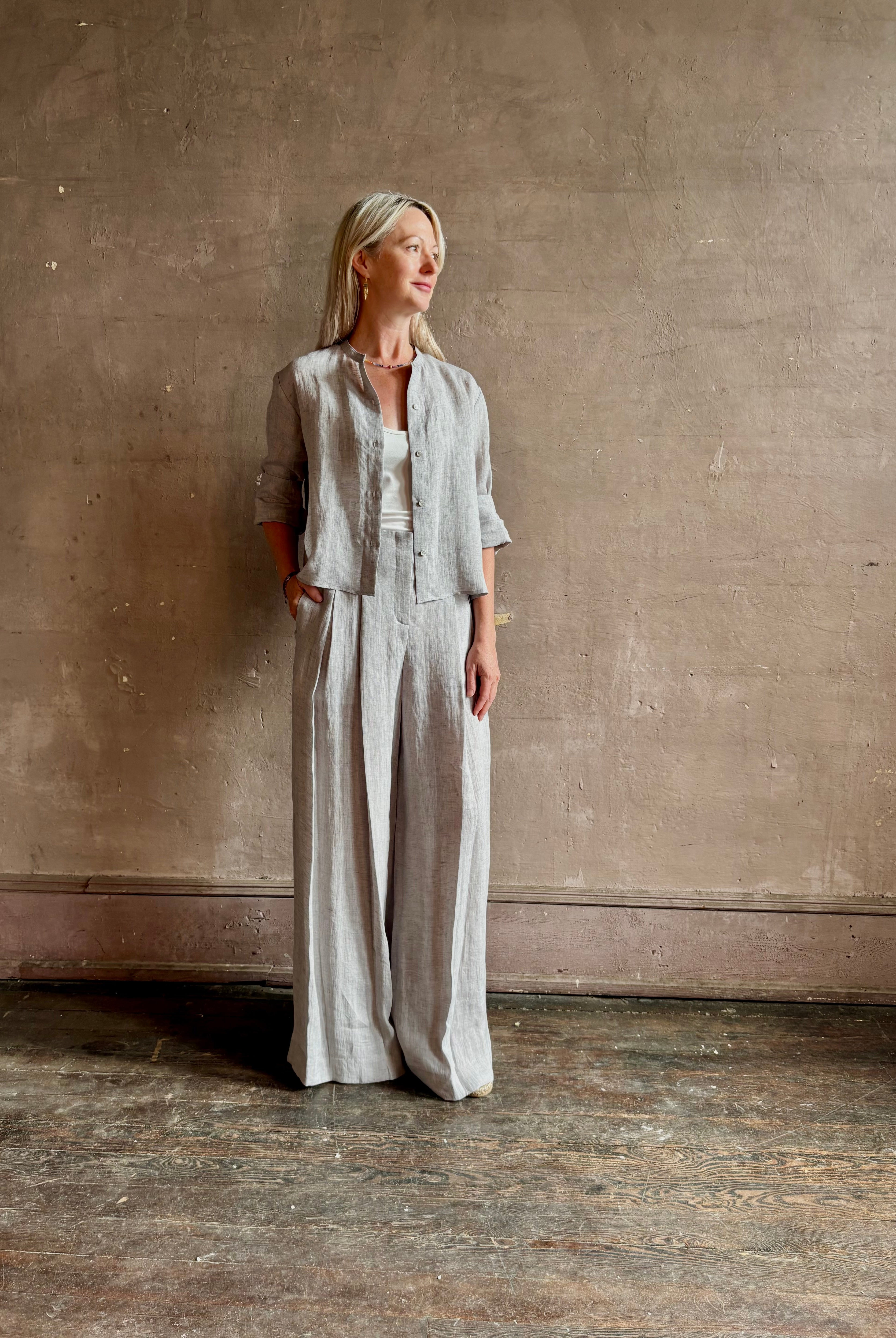 Mature woman wearing Stand Collar Cut Off Top from TWP rendered in a versatile light heather grey and crafted from 100% hemp with round mandarin collar, button front, half sleeves and made in the USA