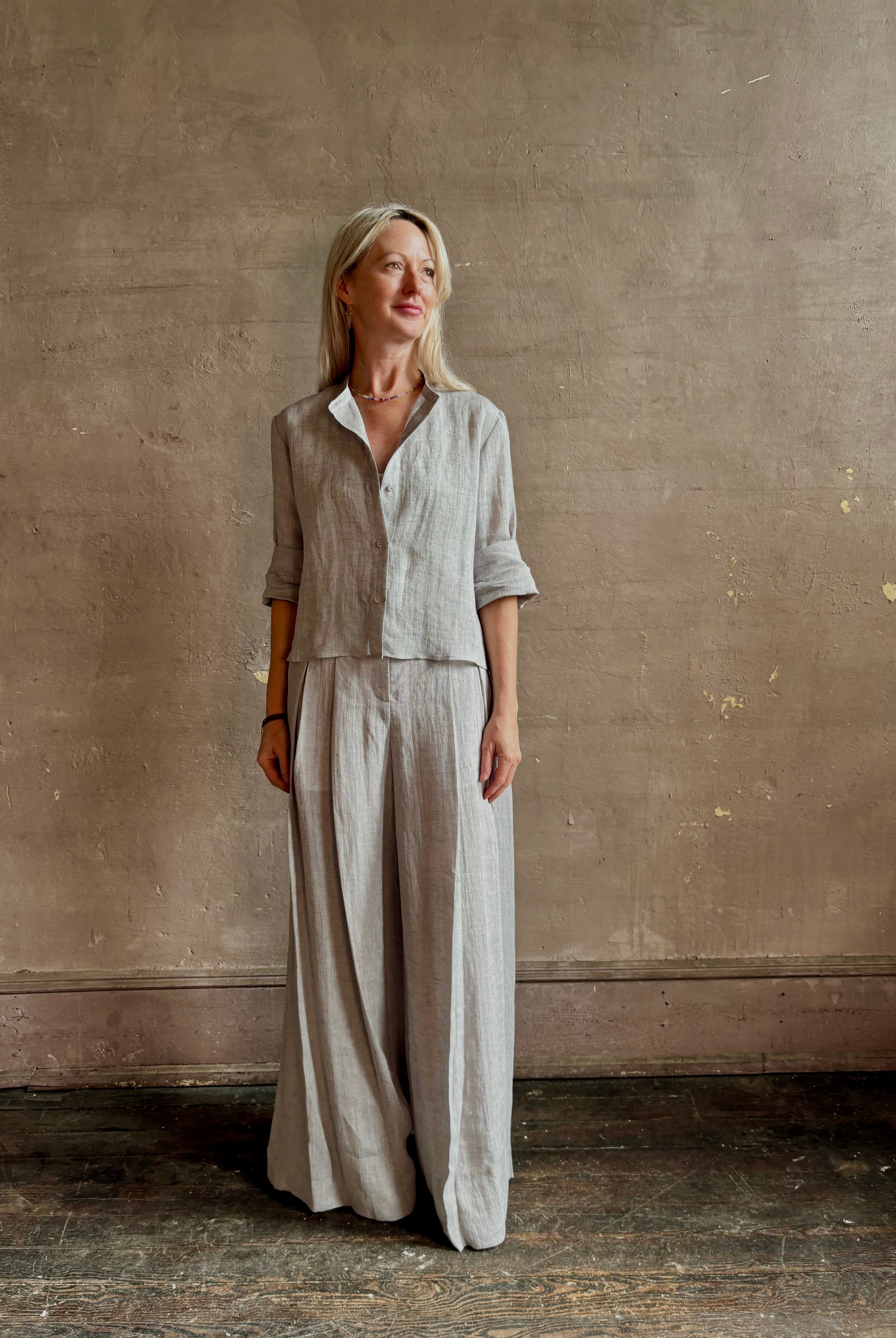 Mature woman wearing Stand Collar Cut Off Top from TWP rendered in a versatile light heather grey and crafted from 100% hemp with round mandarin collar, button front, half sleeves and made in the USA