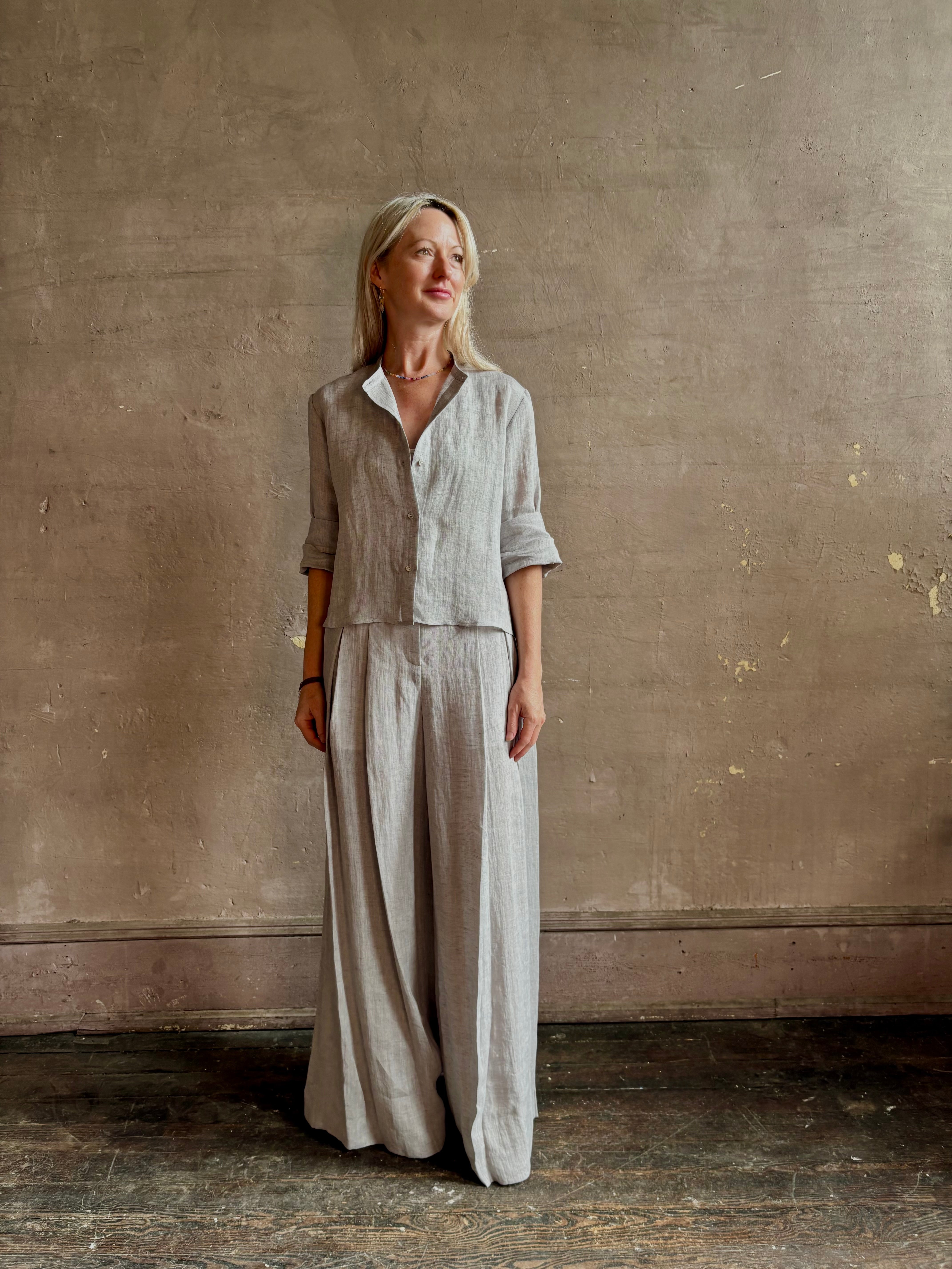 Mature woman wearing Stand Collar Cut Off Top from TWP rendered in a versatile light heather grey and crafted from 100% hemp with round mandarin collar, button front, half sleeves and made in the USA