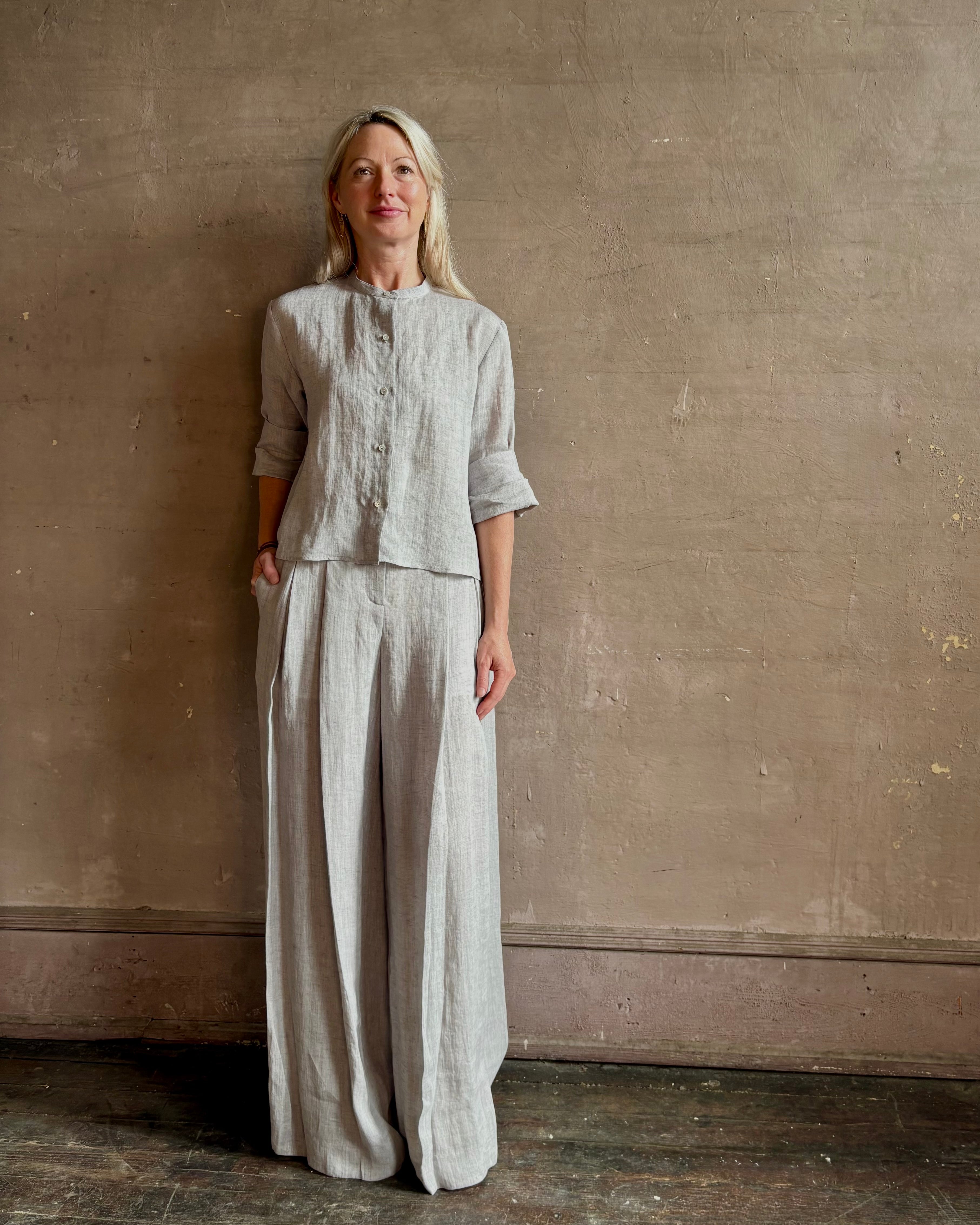 Mature woman wearing Stand Collar Cut Off Top from TWP rendered in a versatile light heather grey and crafted from 100% hemp with round mandarin collar, button front, half sleeves and made in the USA