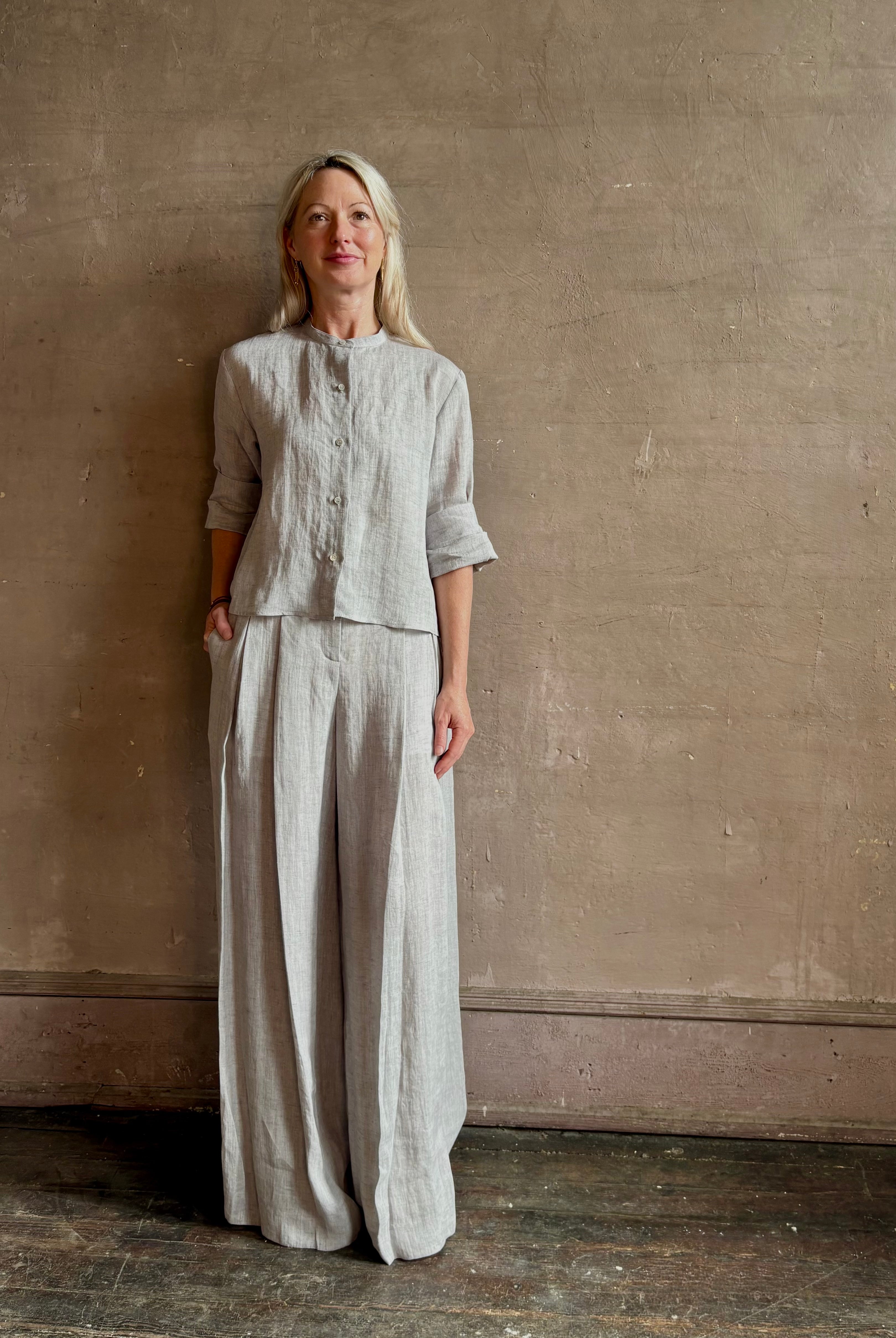 Mature woman wearing Stand Collar Cut Off Top from TWP rendered in a versatile light heather grey and crafted from 100% hemp with round mandarin collar, button front, half sleeves and made in the USA