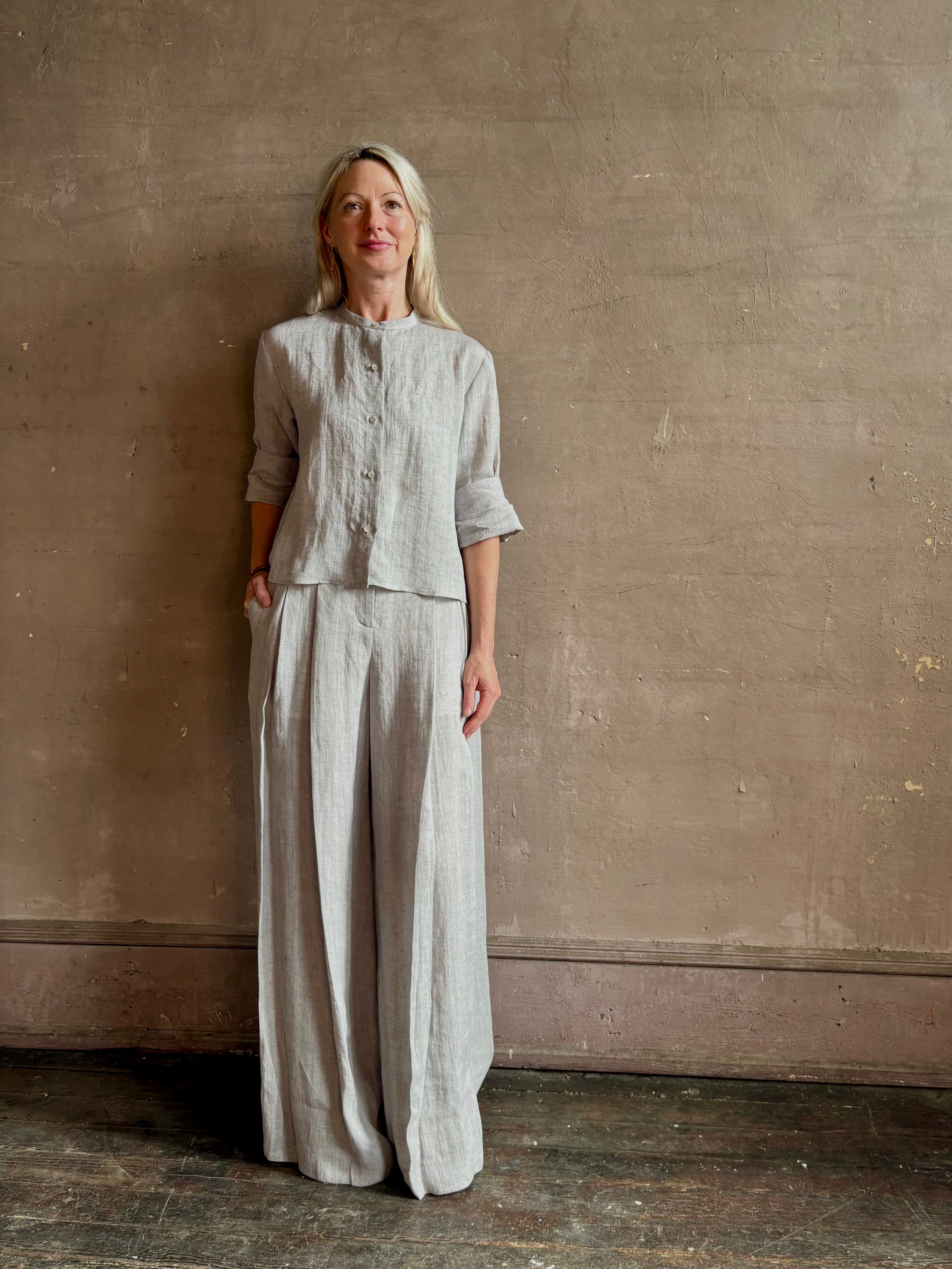 Mature woman wearing Stand Collar Cut Off Top from TWP rendered in a versatile light heather grey and crafted from 100% hemp with round mandarin collar, button front, half sleeves and made in the USA