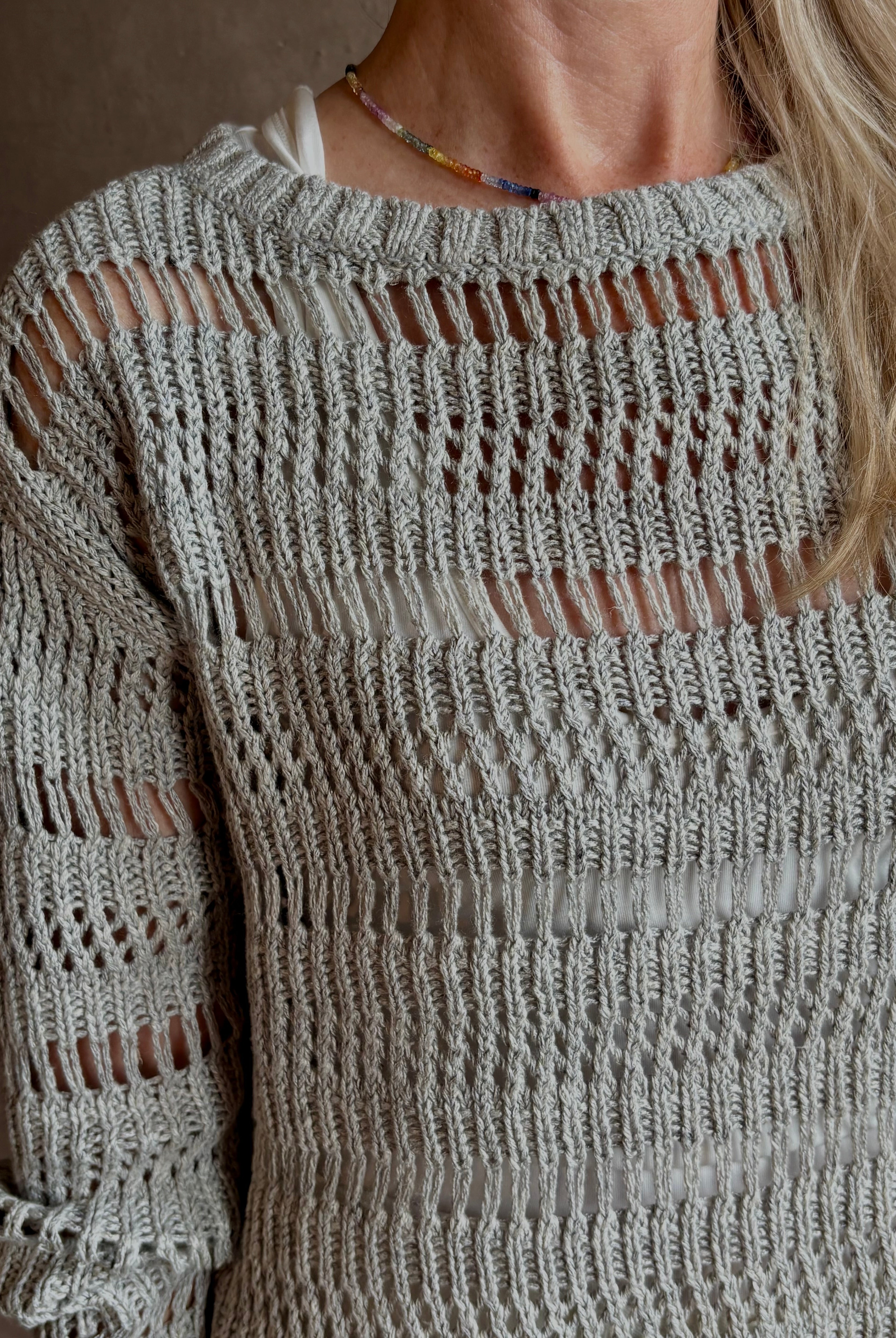 Mature woman wearing Wide Neck Long Sleeve open knit Sweater from TWP in a luxuriously wearable everyday essential rendered in a soft light grey and crafted from an elevated blend of European flax linen and recycled mulberry silk