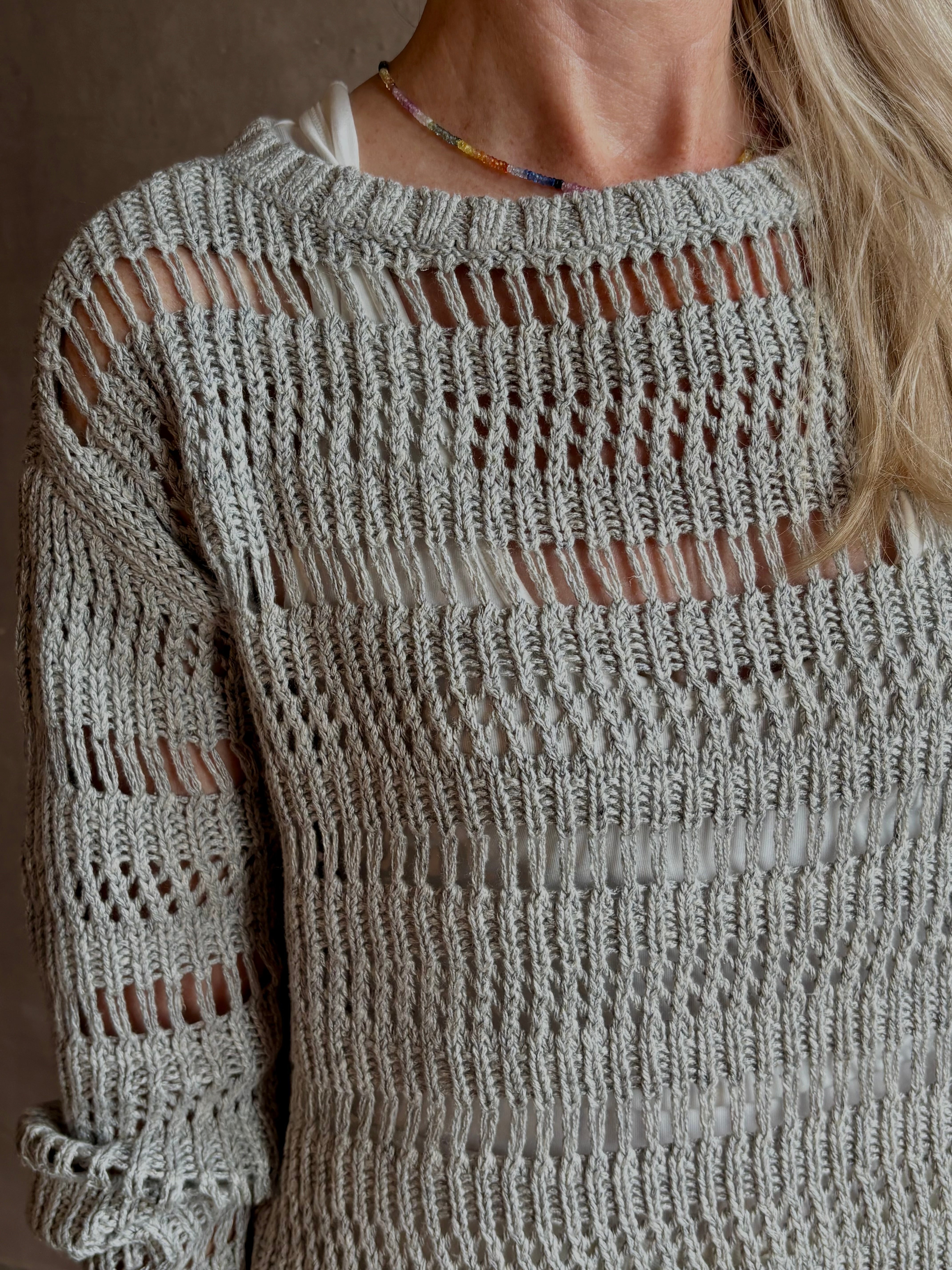 Mature woman wearing Wide Neck Long Sleeve open knit Sweater from TWP in a luxuriously wearable everyday essential rendered in a soft light grey and crafted from an elevated blend of European flax linen and recycled mulberry silk
