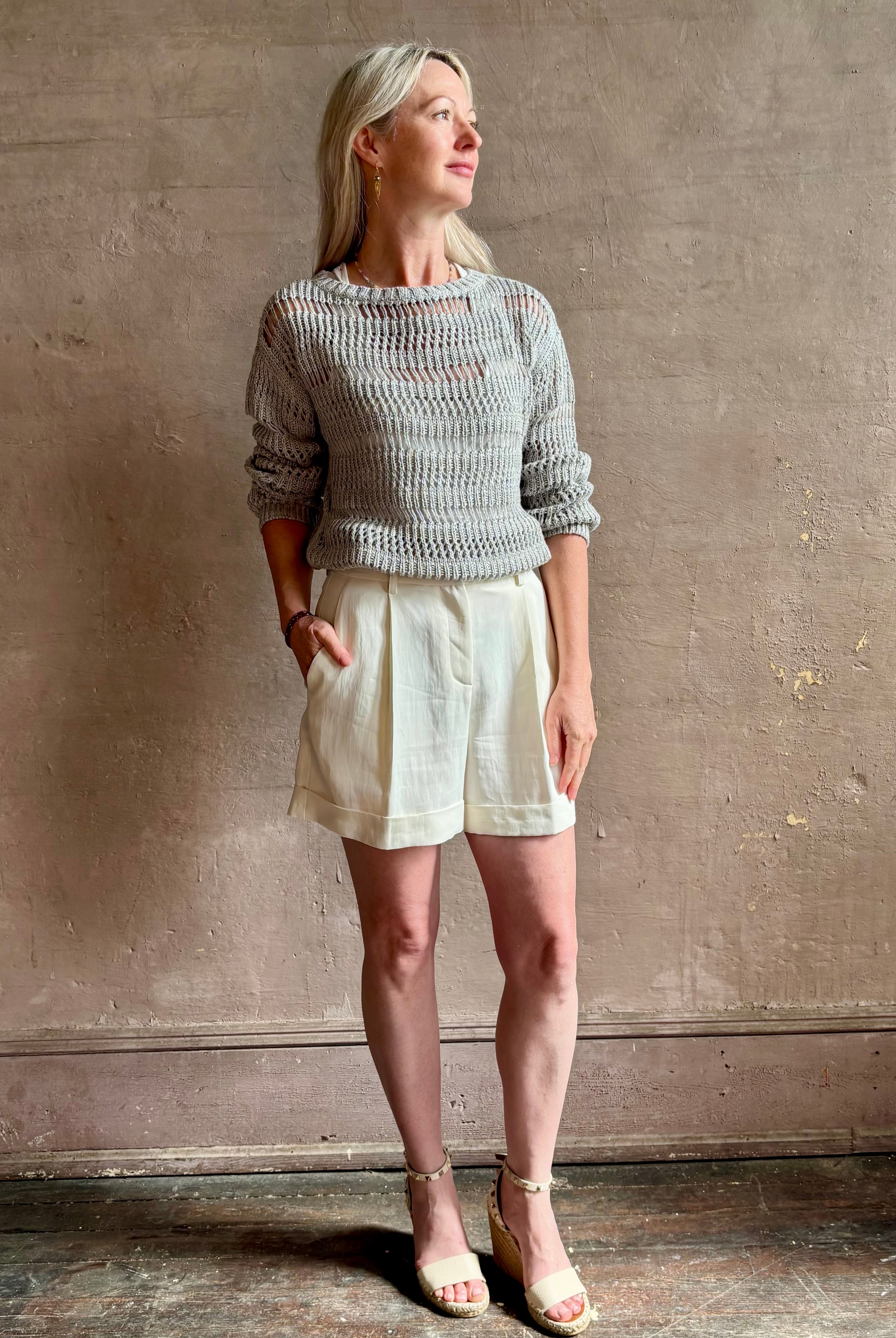 Mature woman wearing Wide Neck Long Sleeve open knit Sweater from TWP in a luxuriously wearable everyday essential rendered in a soft light grey and crafted from an elevated blend of European flax linen and recycled mulberry silk