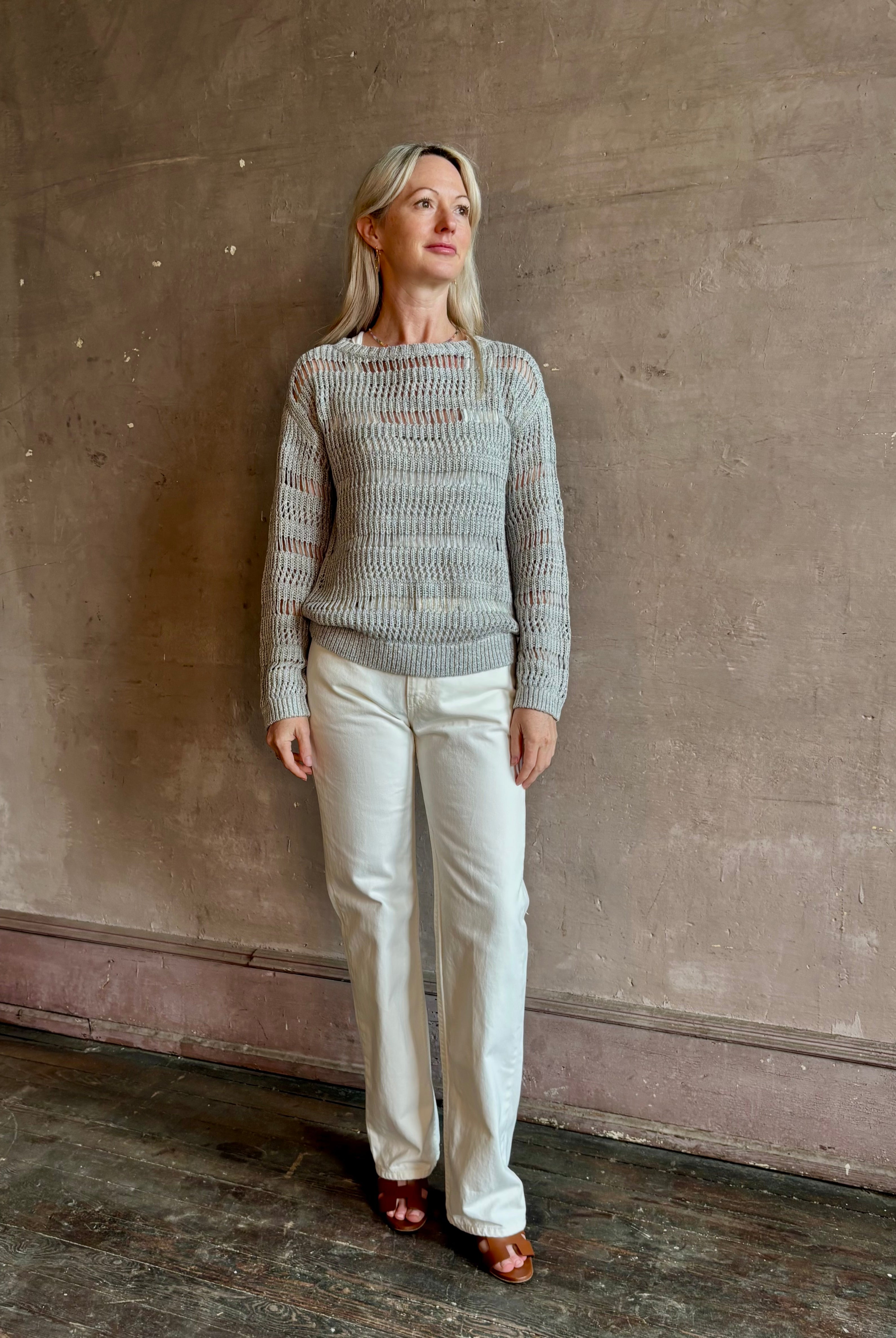 Mature woman wearing Wide Neck Long Sleeve open knit Sweater from TWP in a luxuriously wearable everyday essential rendered in a soft light grey and crafted from an elevated blend of European flax linen and recycled mulberry silk
