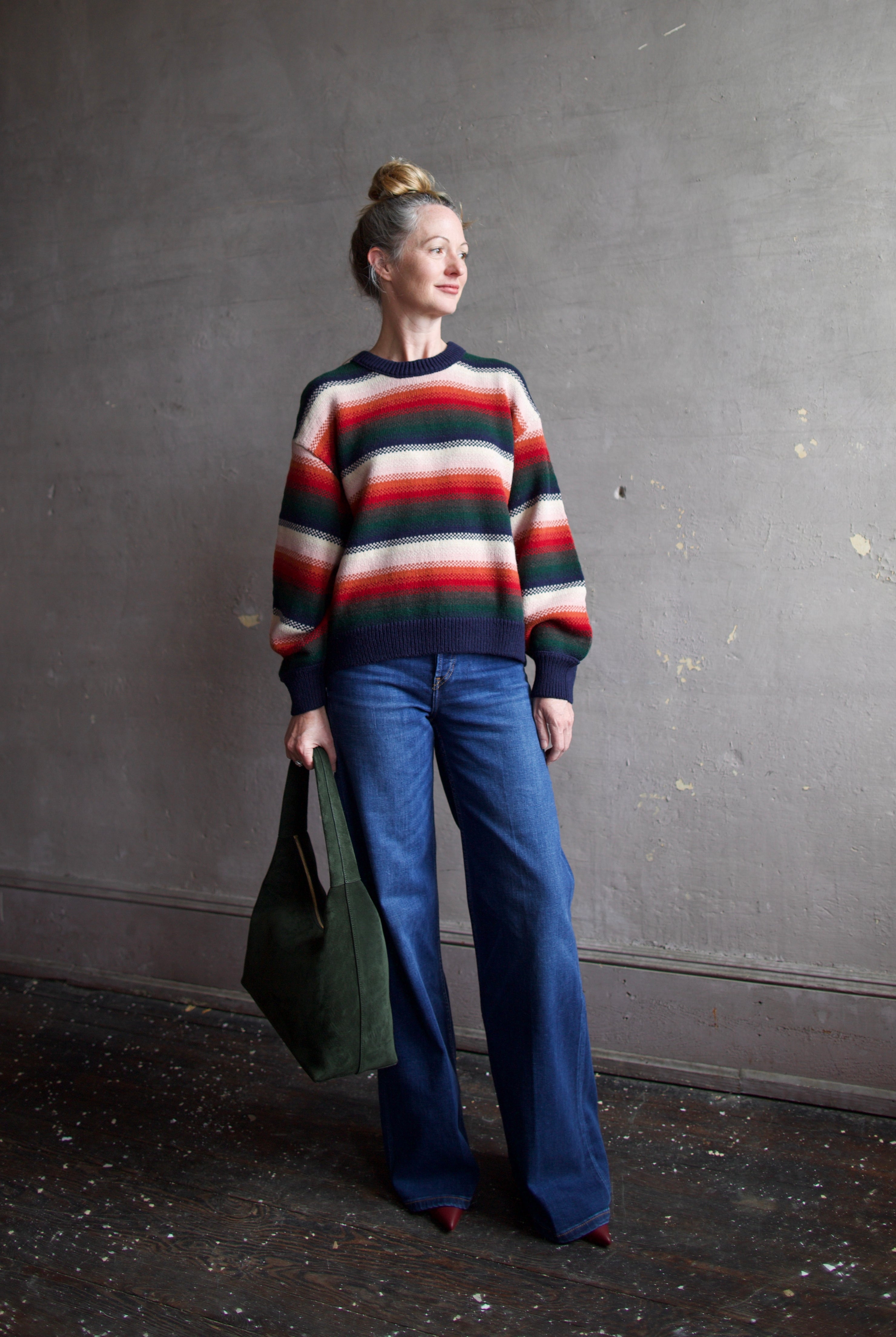 Image featuring a woman wearing the Bubble pullover sweater by The Great with a crew neckline, boxy fit, and drop shoulder in a navy, green, red, and cream stripe.