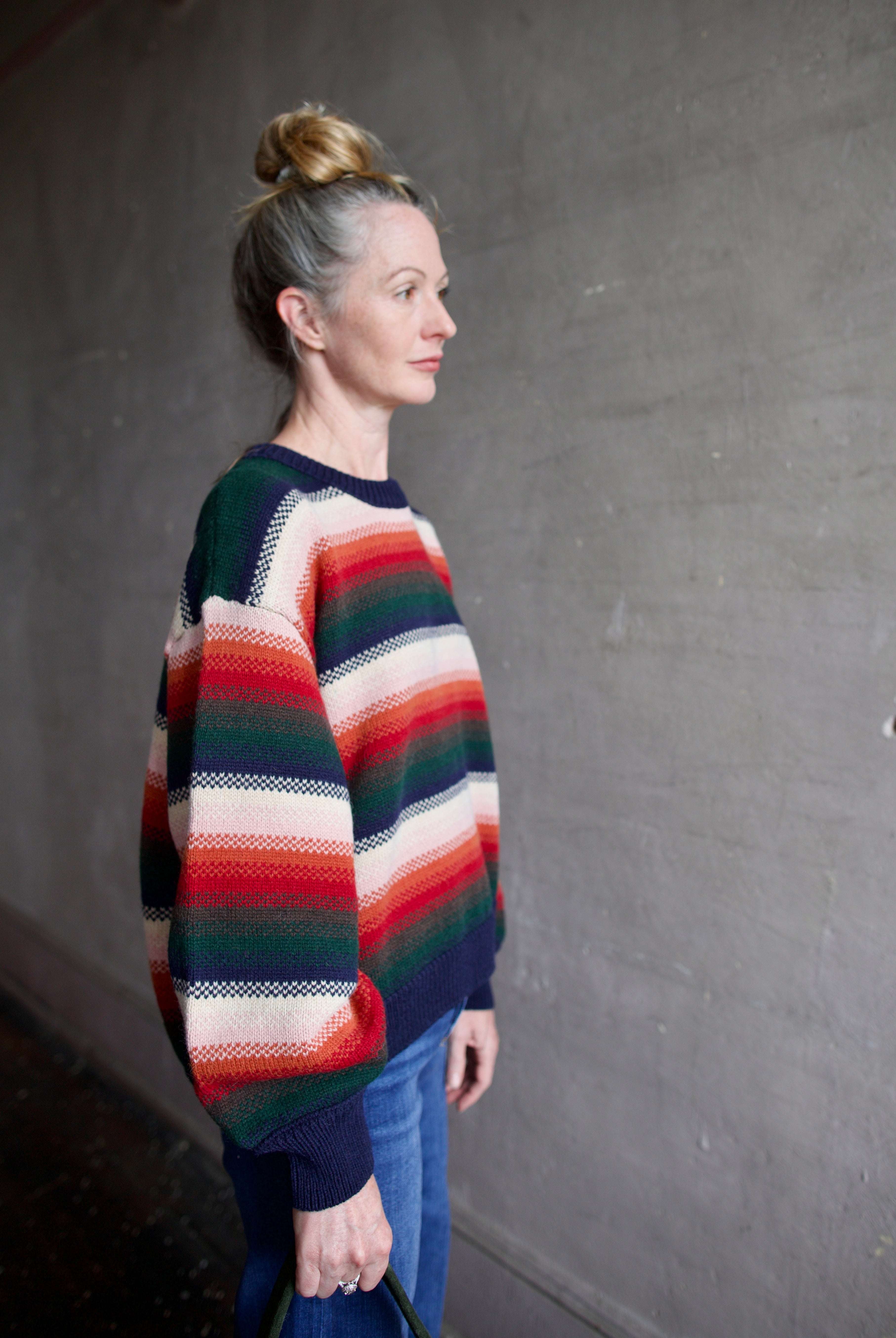 Image featuring a woman wearing the Bubble pullover sweater by The Great with a crew neckline, boxy fit, and drop shoulder in a navy, green, red, and cream stripe.