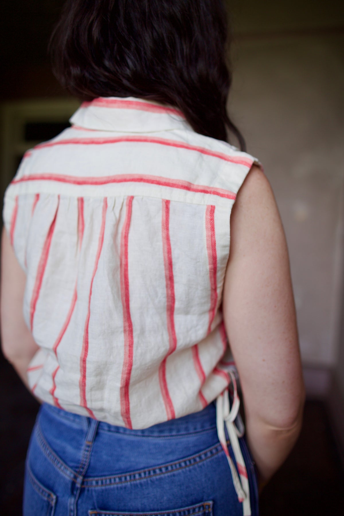 Woman wearing Trovata Ivy cream and pink striped linen Shirt in Pomme Stripe button front, drawstring waist, and cropped fit. Sun-faded, playful California ease