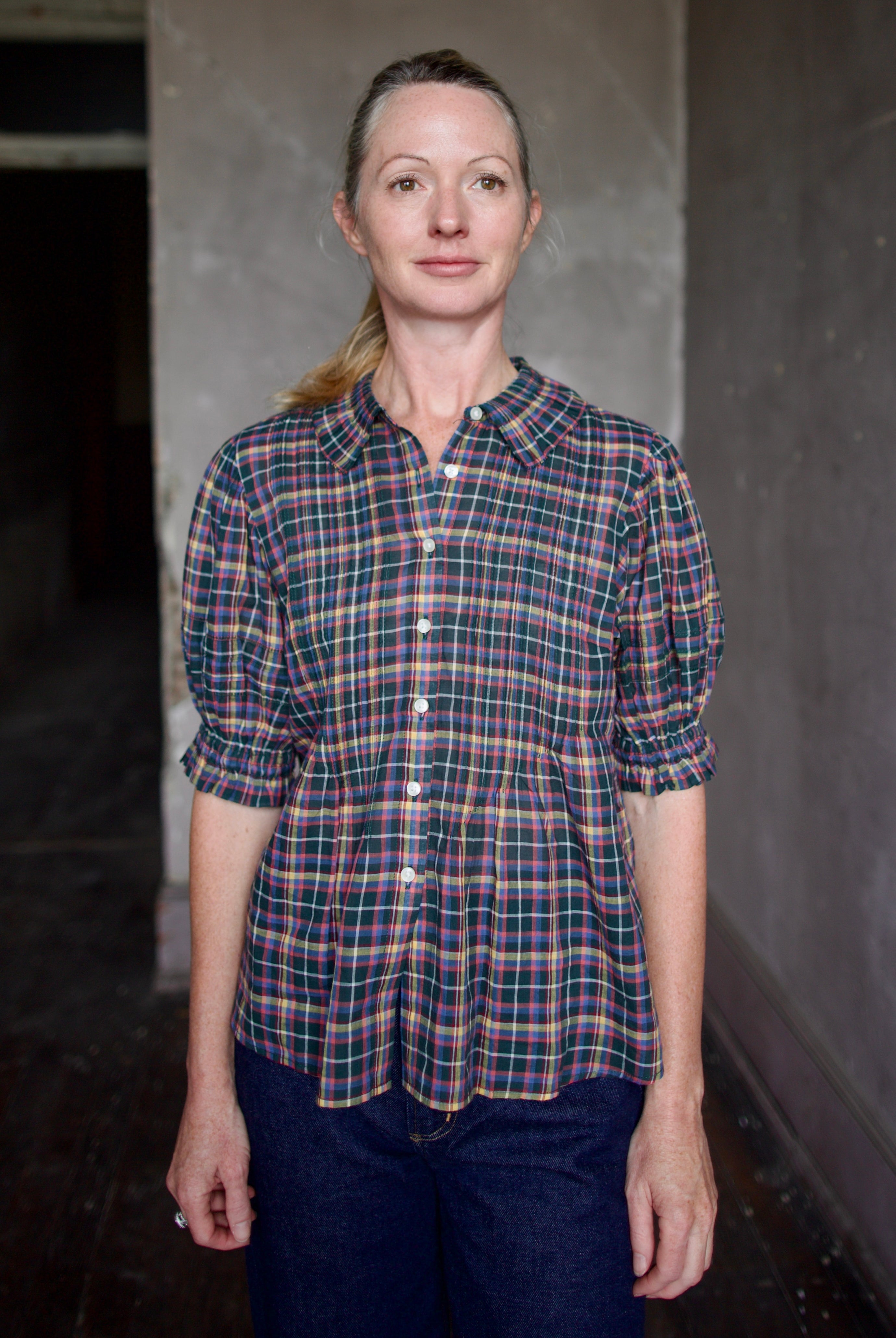 Model wearing Trovata Jess Blouse in cotton plaid with ruffle short sleeve detail pin tucking button front