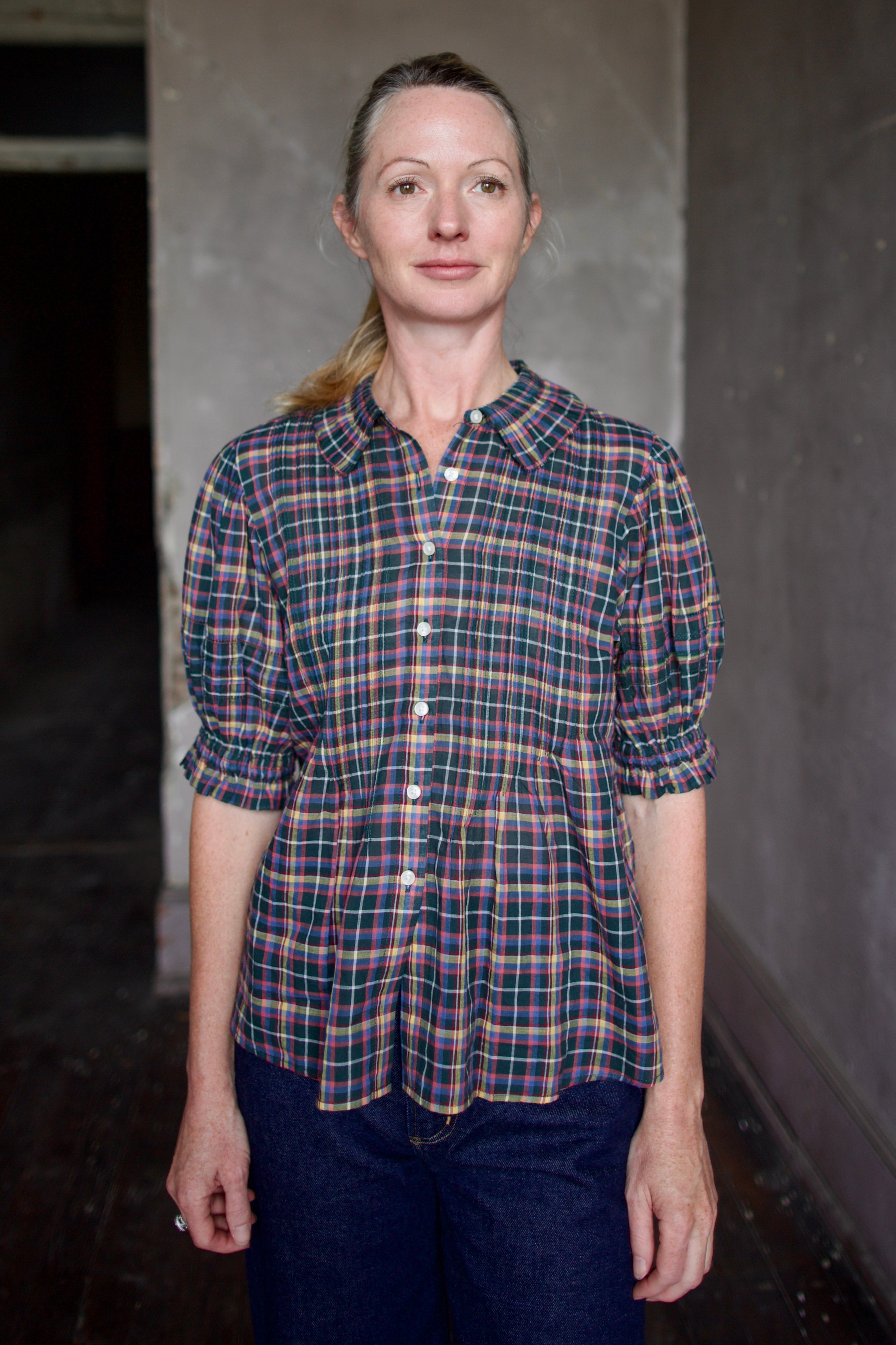 Model wearing Trovata Jess Blouse in cotton plaid with ruffle short sleeve detail pin tucking button front