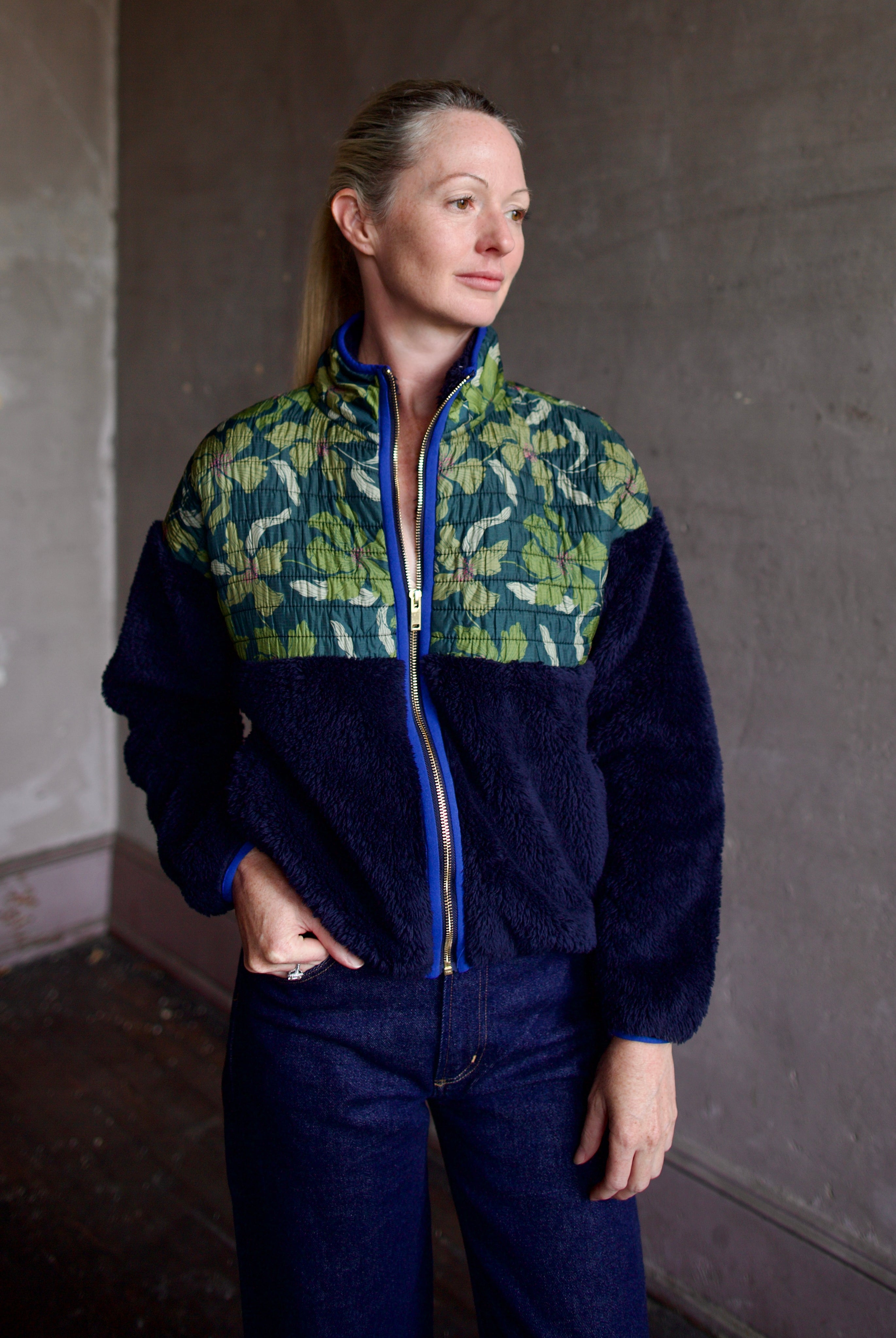 Model wearing a Trovata Lennox zip-up fleece jacket in navy with a fauna green patterned panel and gold zipper