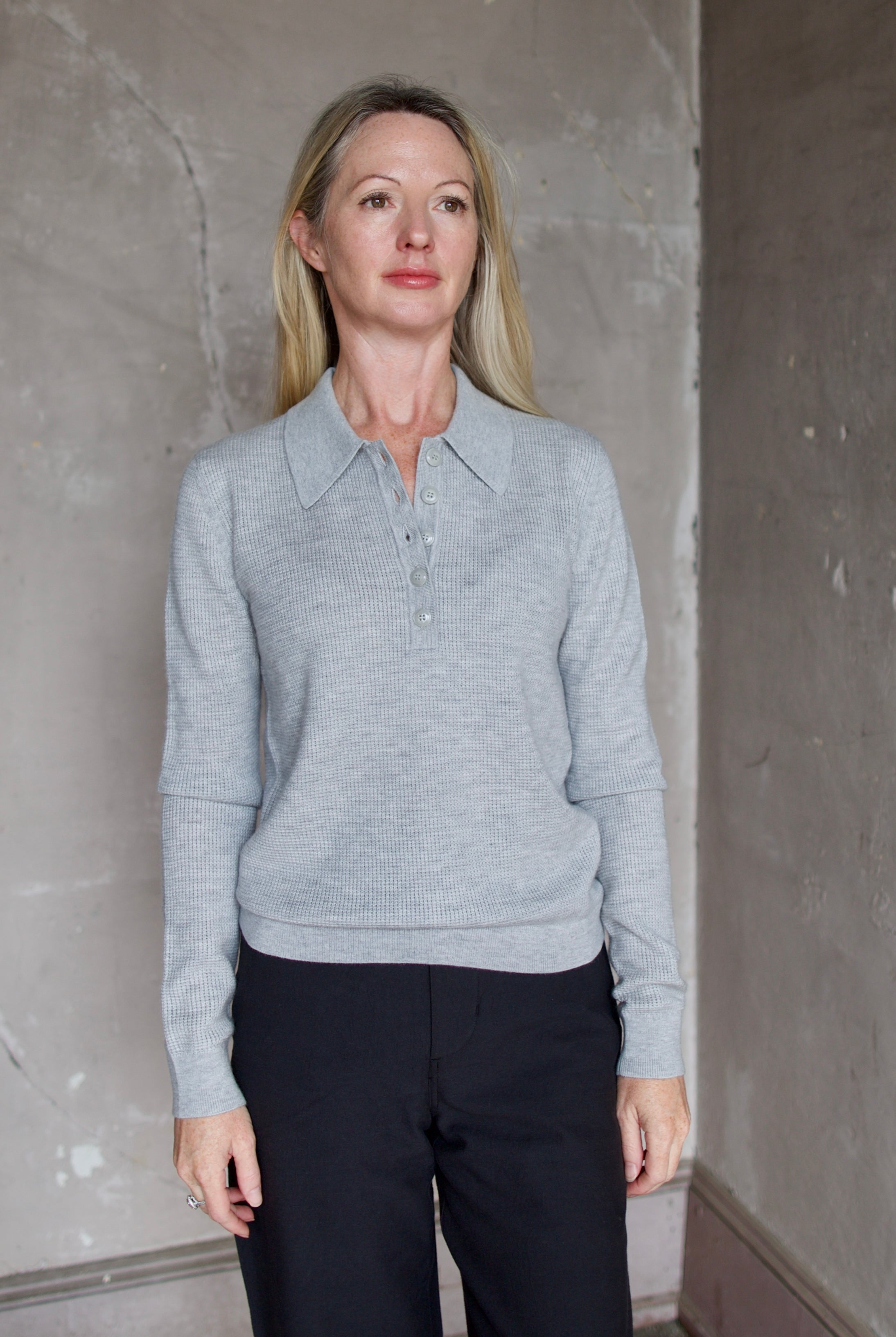 Model wearing TWP Jorden Polo in Light Heather Grey. Henley boasts premium cashmere construction for the ultimate elevated casual look.