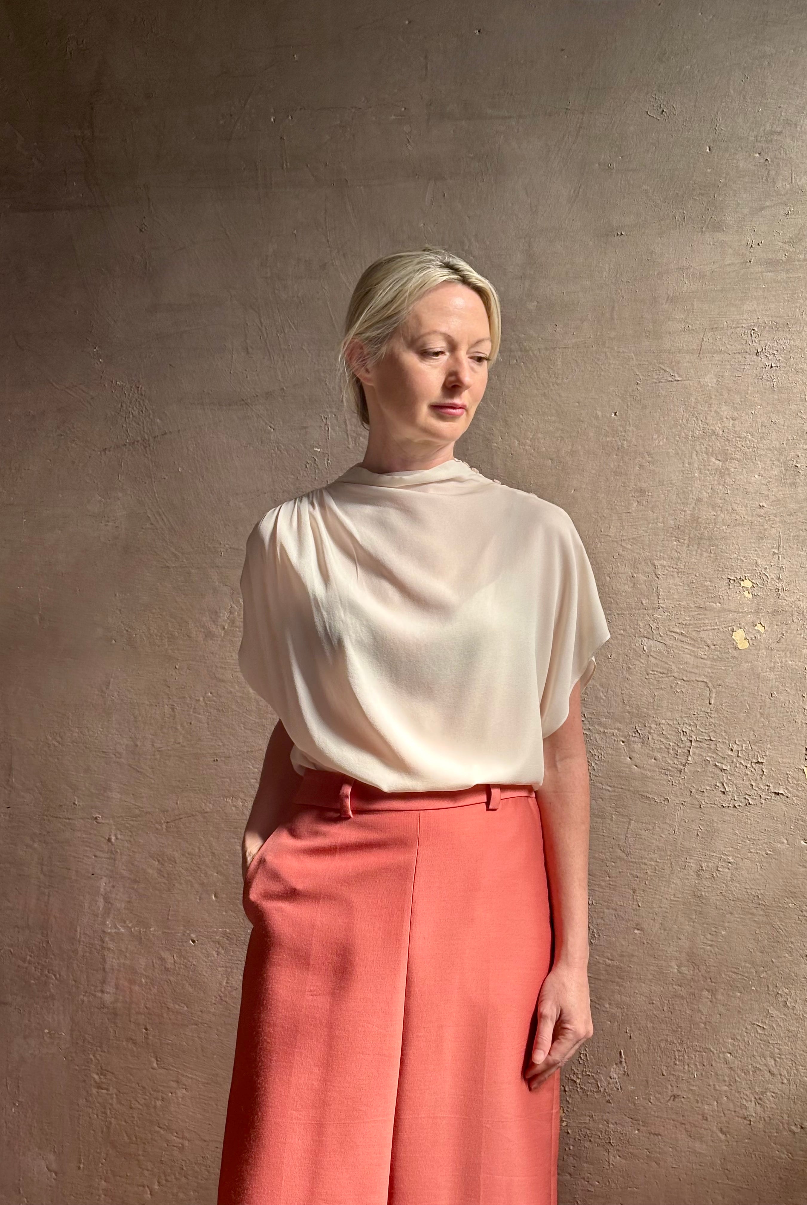 Mature woman wearing an elevated soft blush TWP silk blouse with beautifully draped short sleeves and modern asymmetrical design