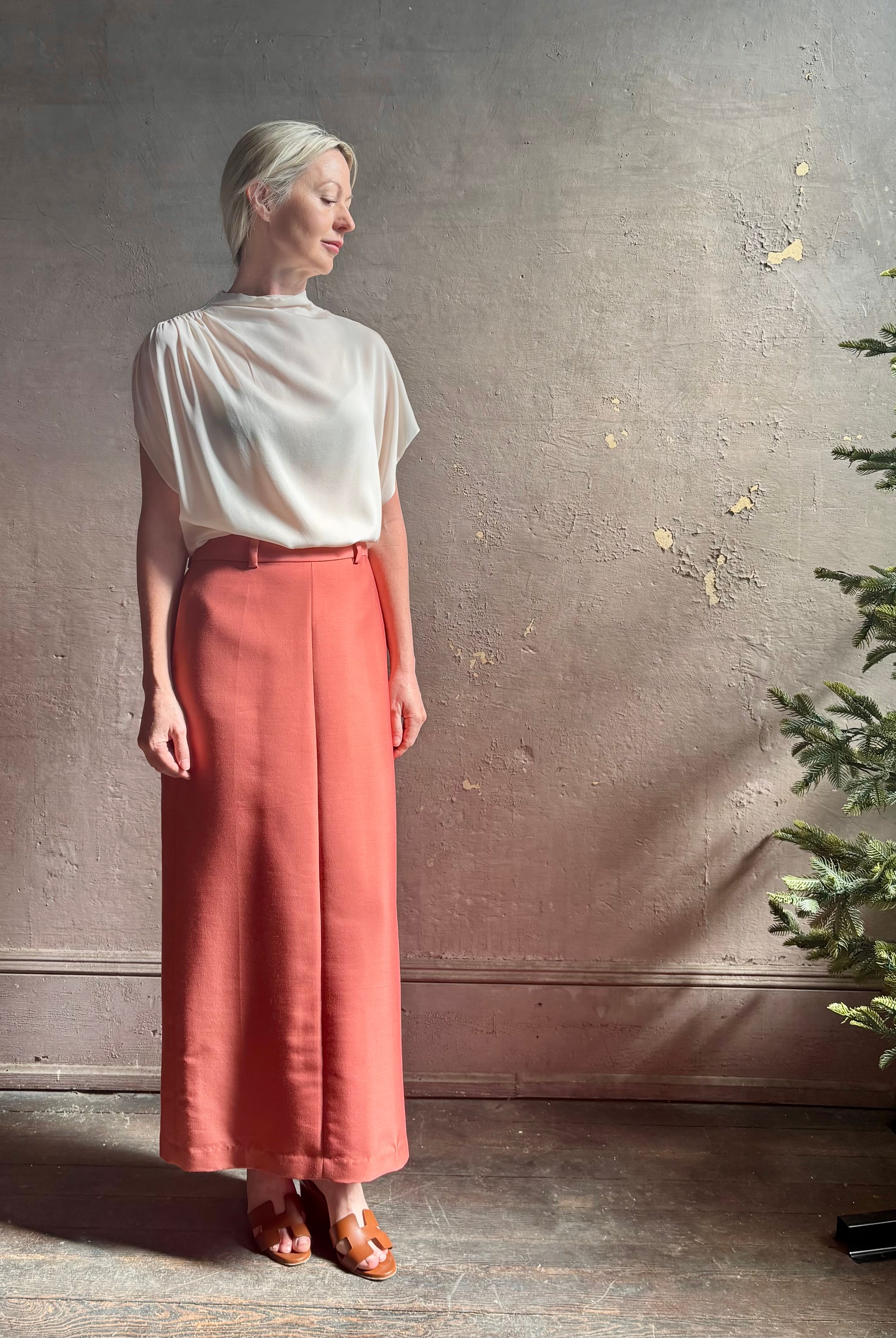 Mature woman wearing an elevated soft blush TWP silk blouse with beautifully draped short sleeves and modern asymmetrical design