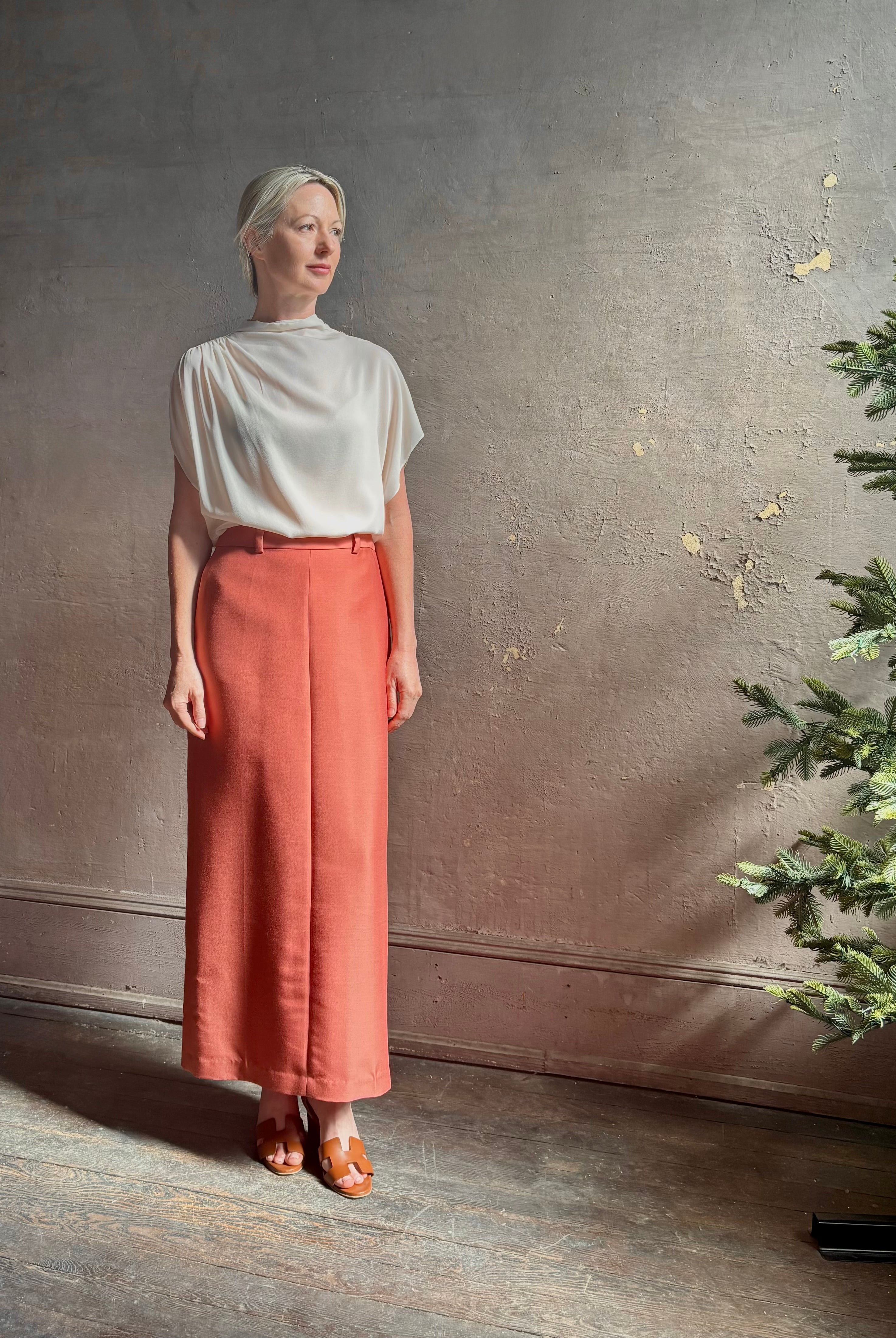 Mature woman wearing an elevated soft blush TWP silk blouse with beautifully draped short sleeves and modern asymmetrical design