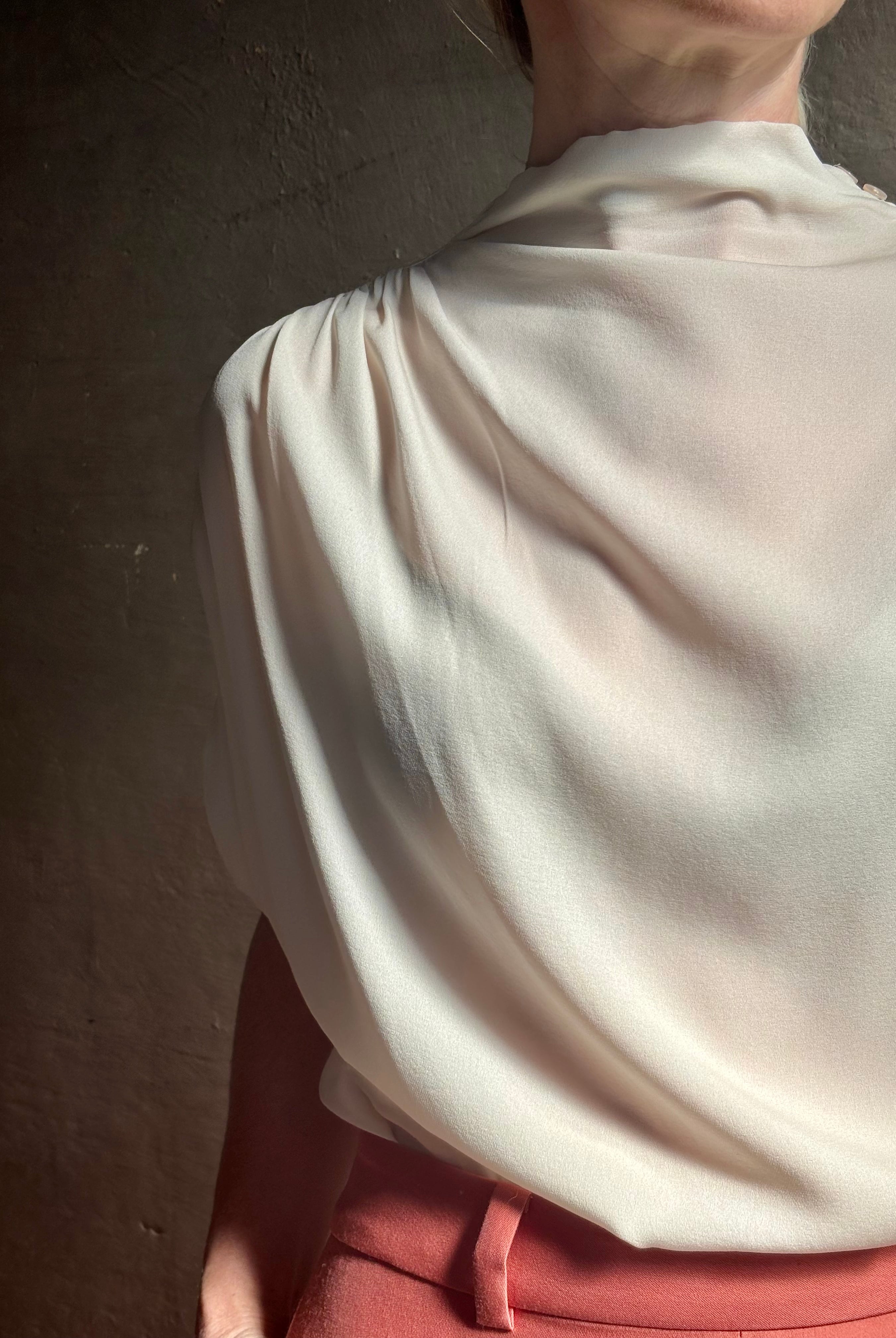 Mature woman wearing an elevated soft blush TWP silk blouse with beautifully draped short sleeves and modern asymmetrical design