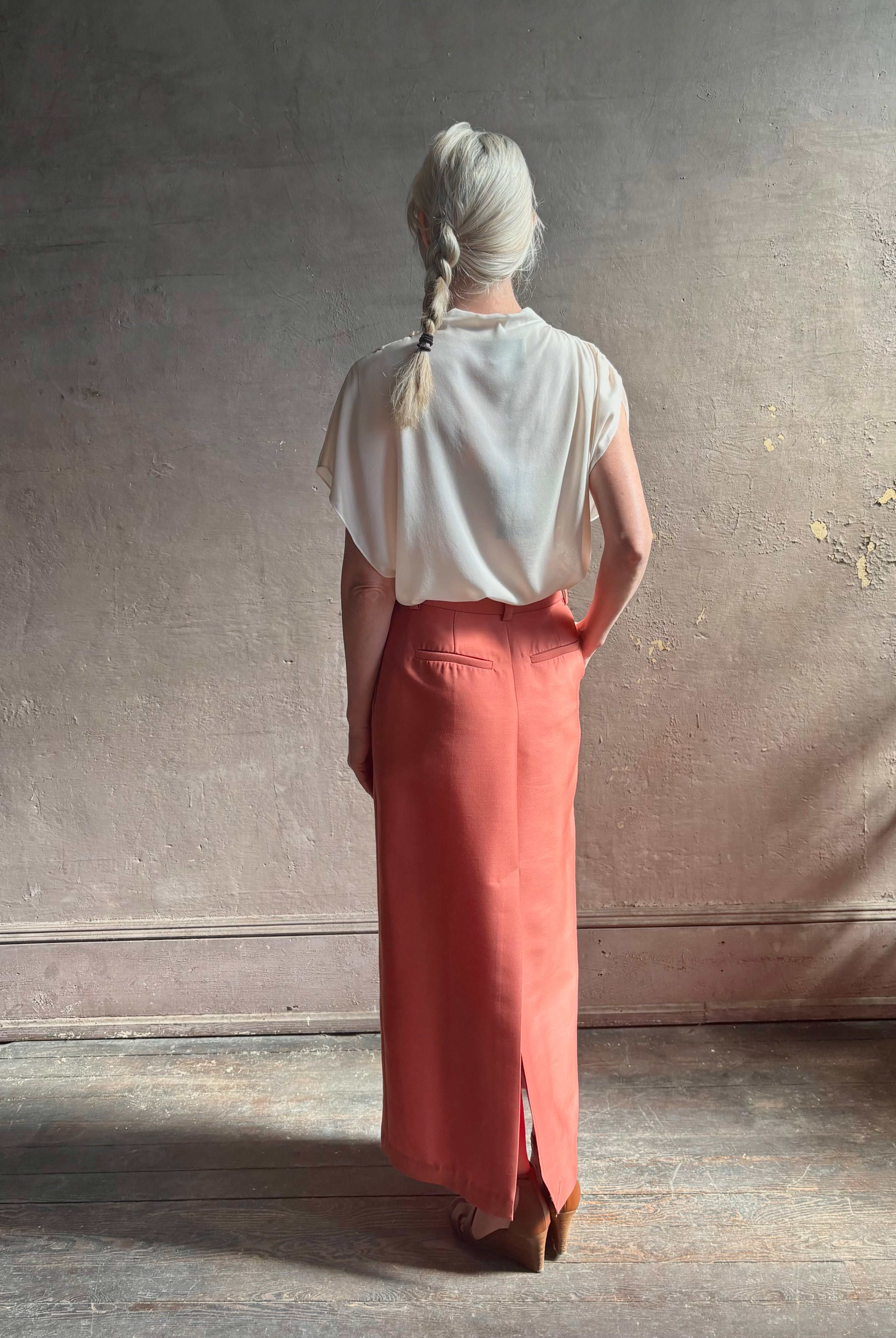 Mature woman wearing an elevated soft blush TWP silk blouse with beautifully draped short sleeves and modern asymmetrical design