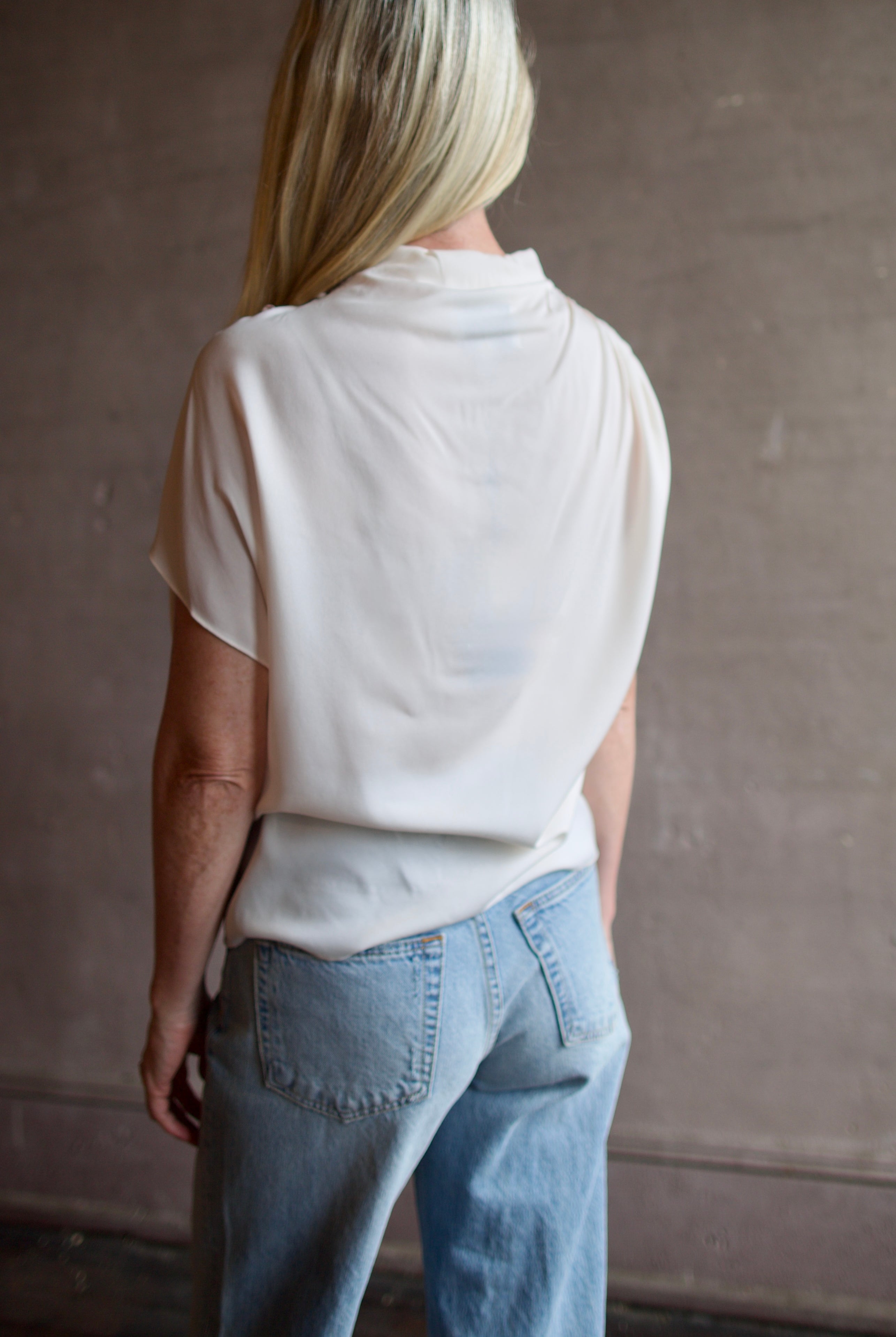 Mature model wearing a blush TWP silk blouse with ruffled sleeves and modern asymmetrical design