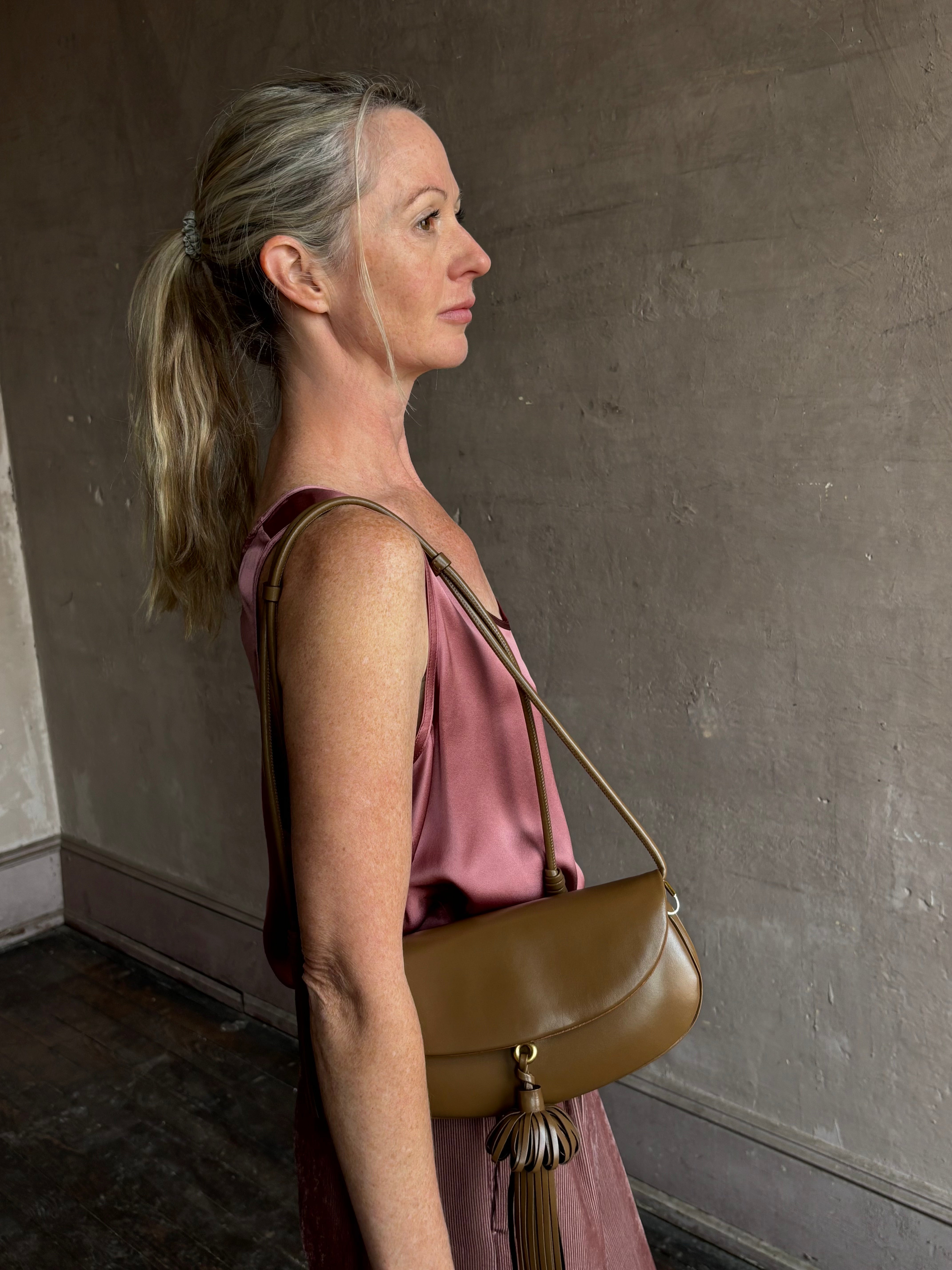 Image of mature model wearing luxury designer ULLA JOHNSON Paloma Tassel Flap leather handbag in rich brown Chestnut